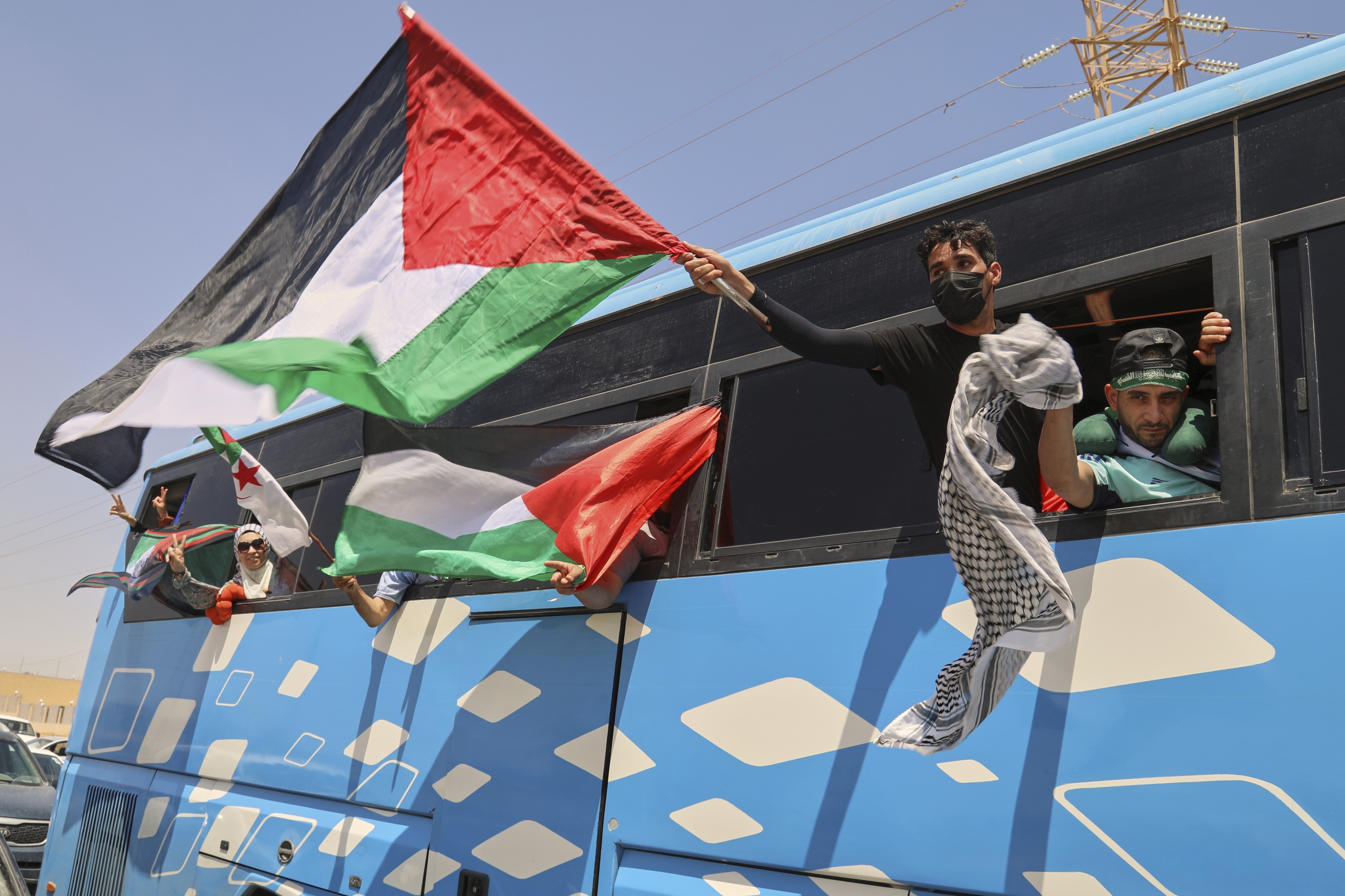 Members of a humanitarian convoy of at least 1,500 people, including activists and supporters from Algeria and Tunisia, wave Palestinian flags from a bus as the group travels toward Gaza via Egypt's Rafah Crossing, in Zawiya, Libya, Tuesday, June 10, 2025. (AP Photo/Yousef Murad)
