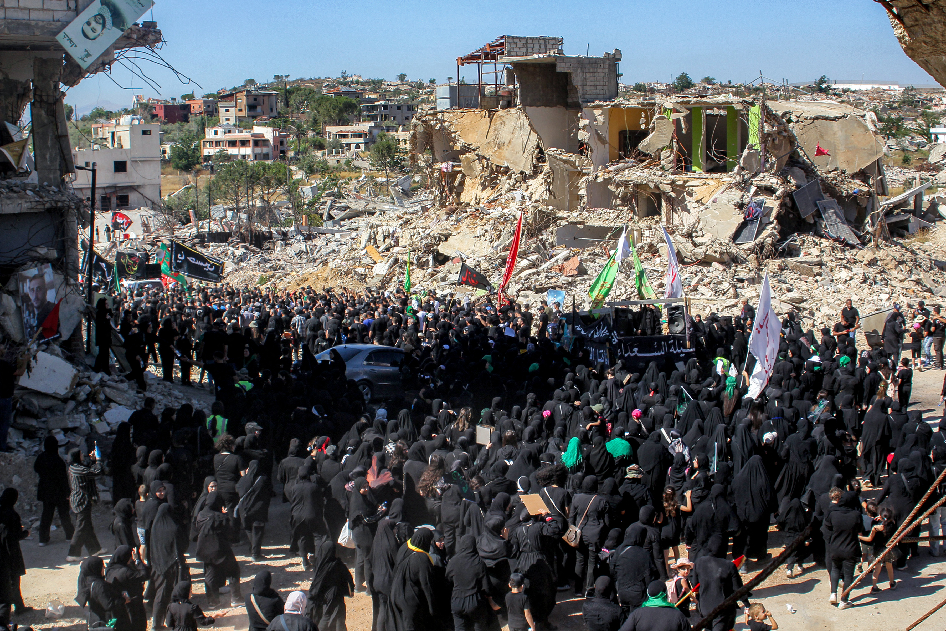 Shiite Muslim worshippers walk past the rubble of buildings destroyed by previous Israeli strikes during a mourning procession in Lebanon's southern village of Kfarkila