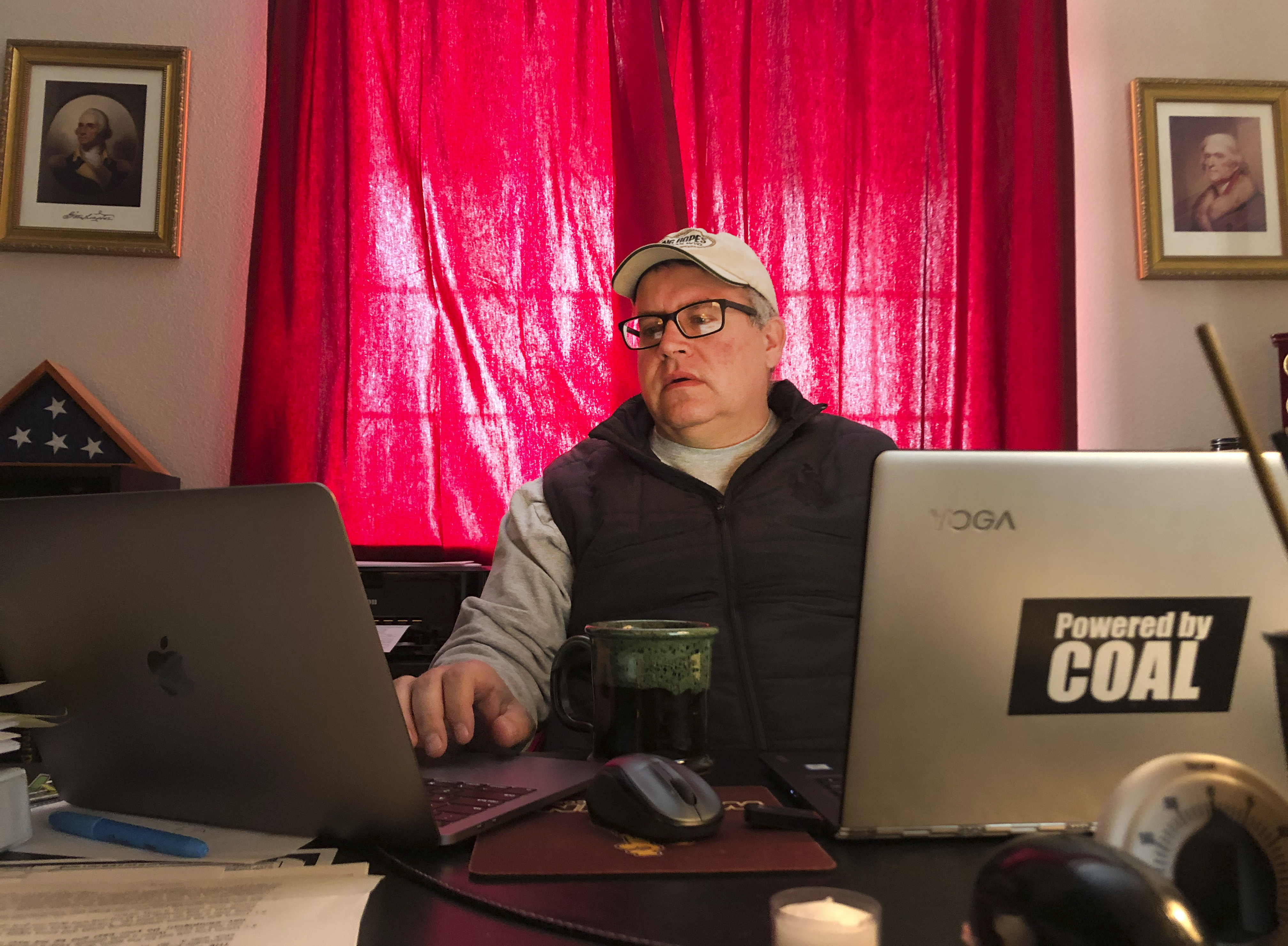 Travis Deti sits in front of his computer, which has a sticker that reads,