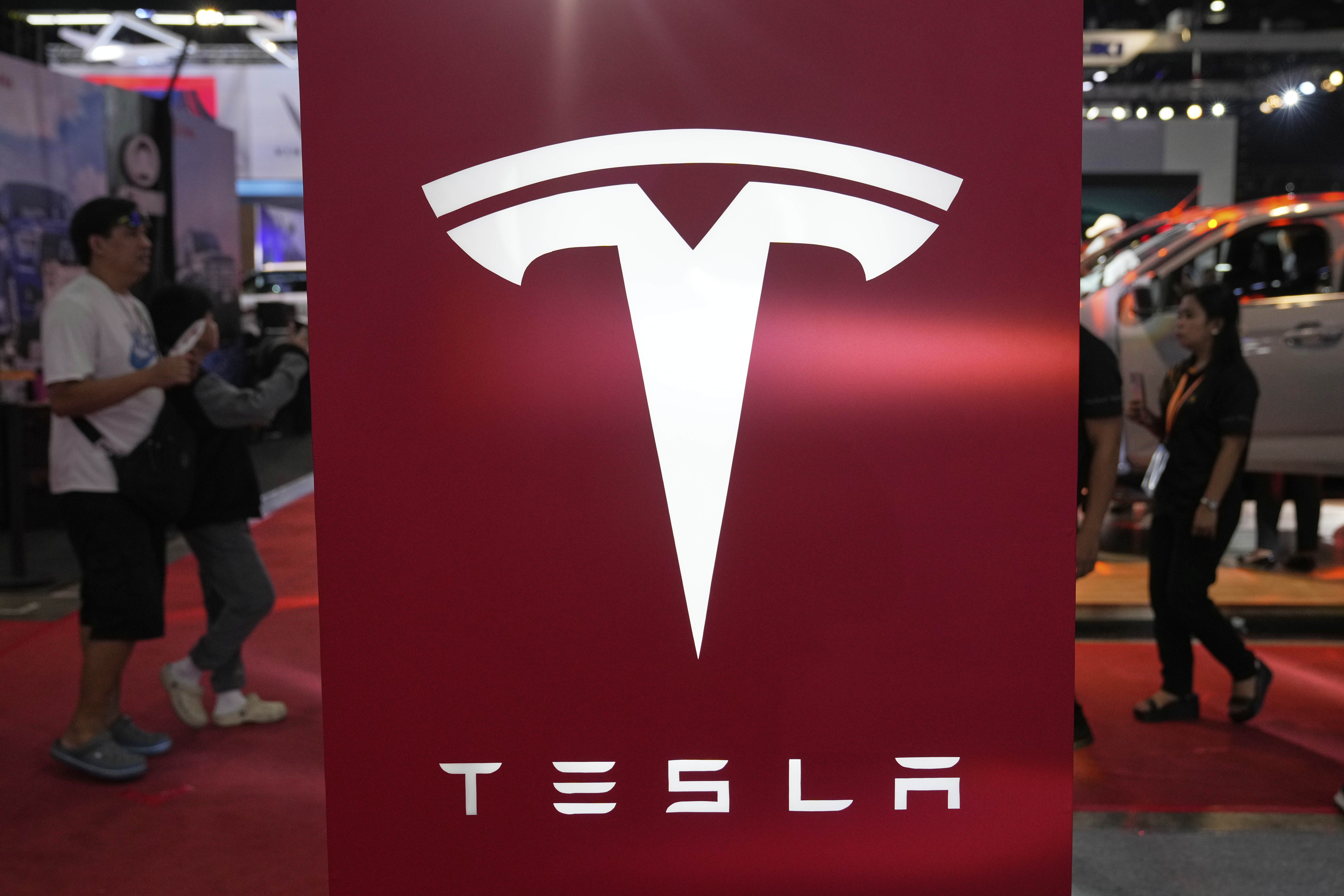 People pass by a Tesla sign at the Manila International Auto Show in Pasay city, Philippines Friday, April 11, 2025. (AP Photo/Aaron Favila)
