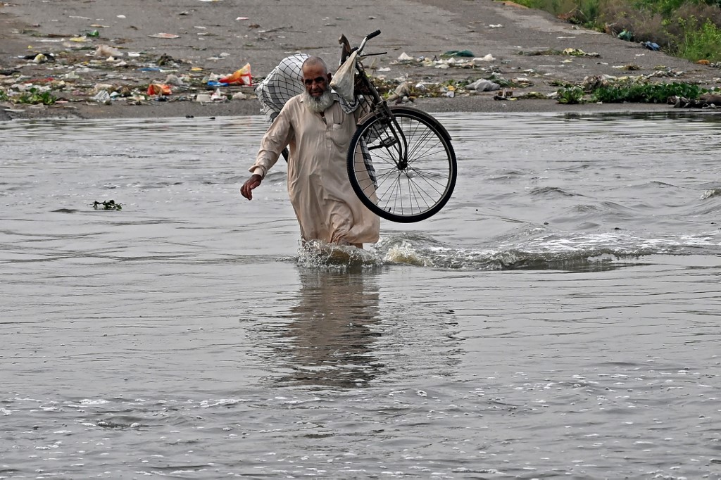 A man carries his bicycle as he wades along a flooded road after heavy monsoon rains in Karachi on August 20, 2025. [Rizwan Tabassum/AFP]