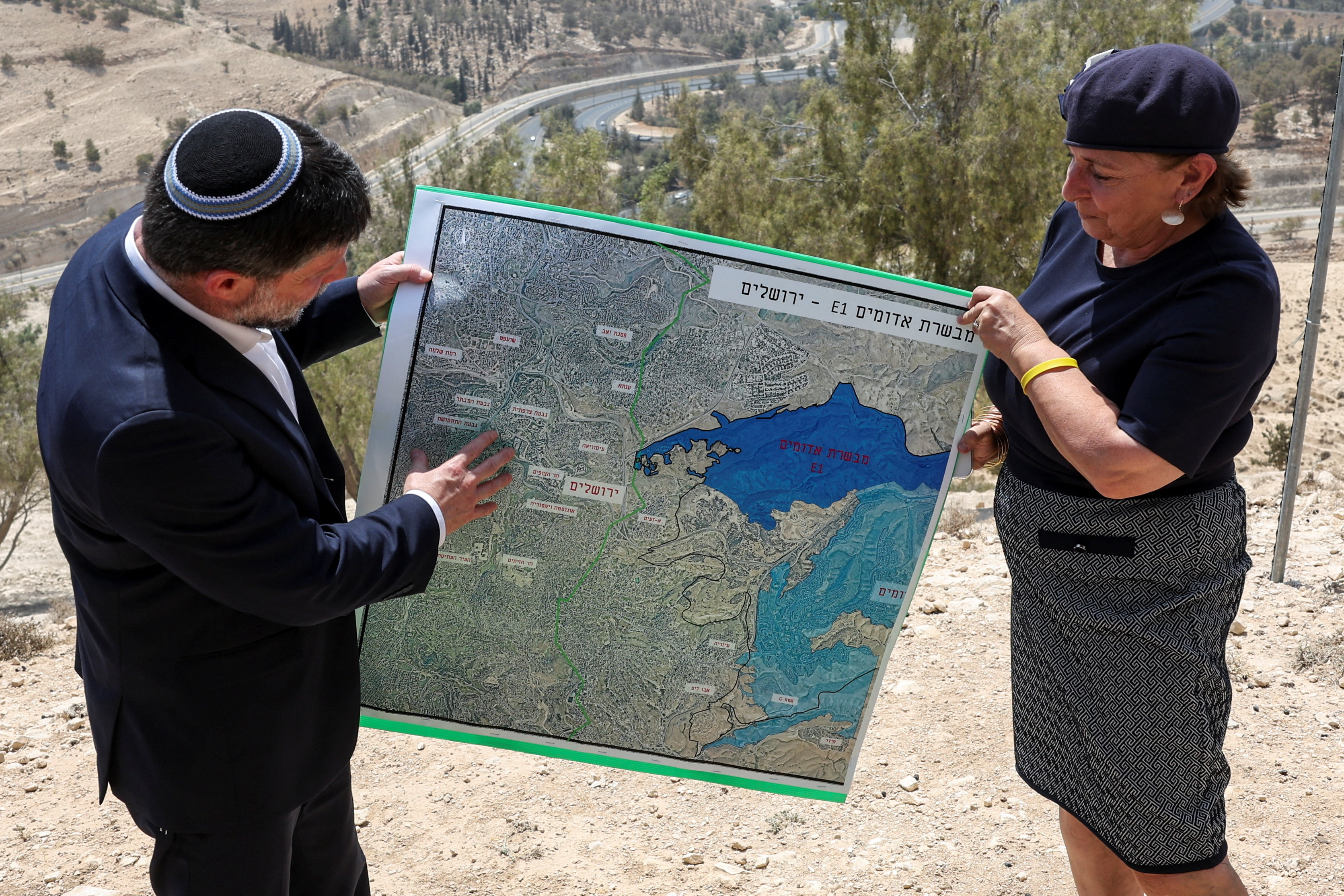 Israeli Finance Minister Bezalel Smotrich and a woman hold a map that shows the long-frozen E1 settlement scheme, that would split East Jerusalem from the occupied West Bank, on the day of a press conference near the Israeli settlement of Maale Adumim, in the Israeli-occupied West Bank, August 14, 2025. REUTERS/Ronen Zvulun