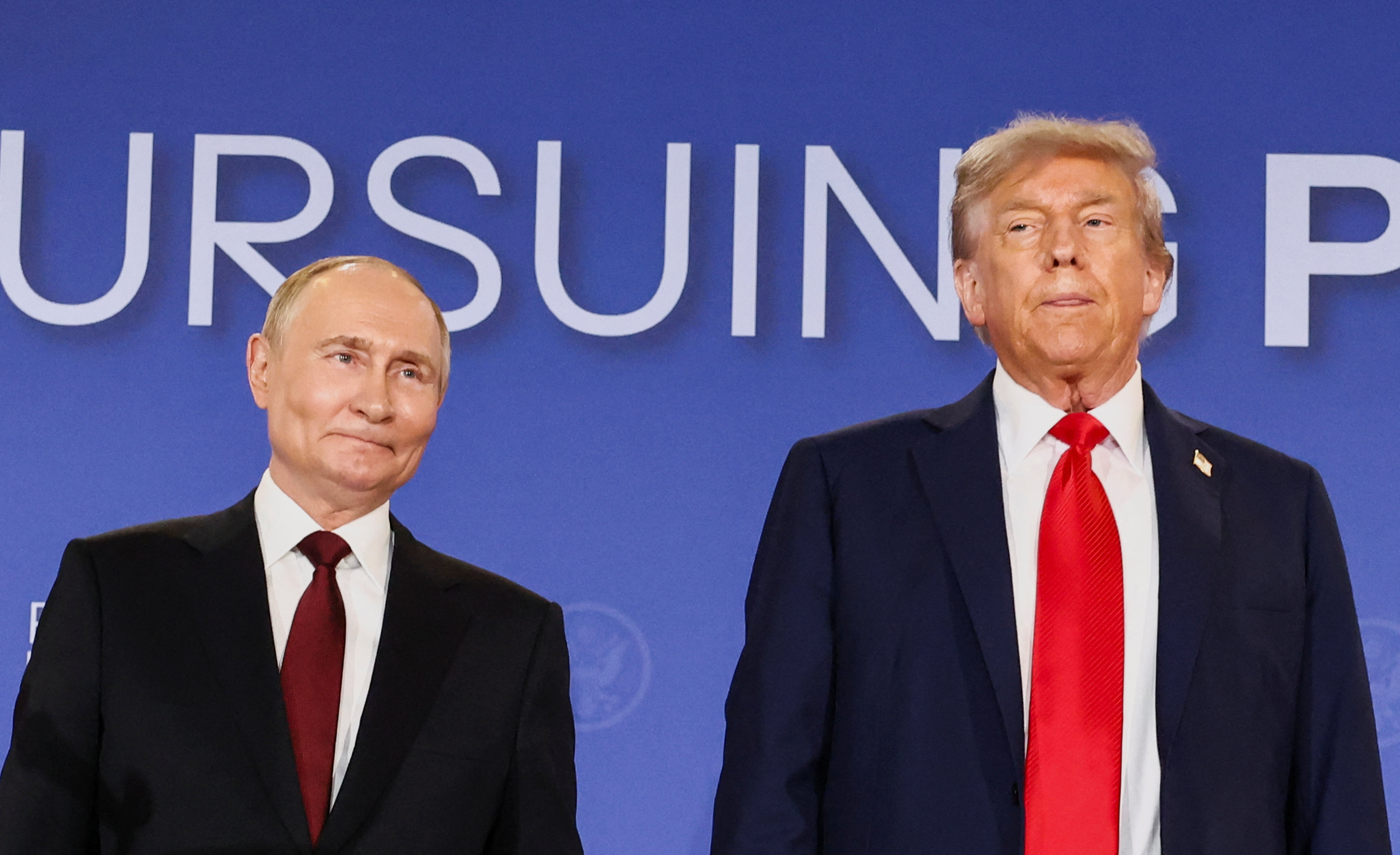 Trump and Putin stand side by side in front of "Pursuing Peace" sign.