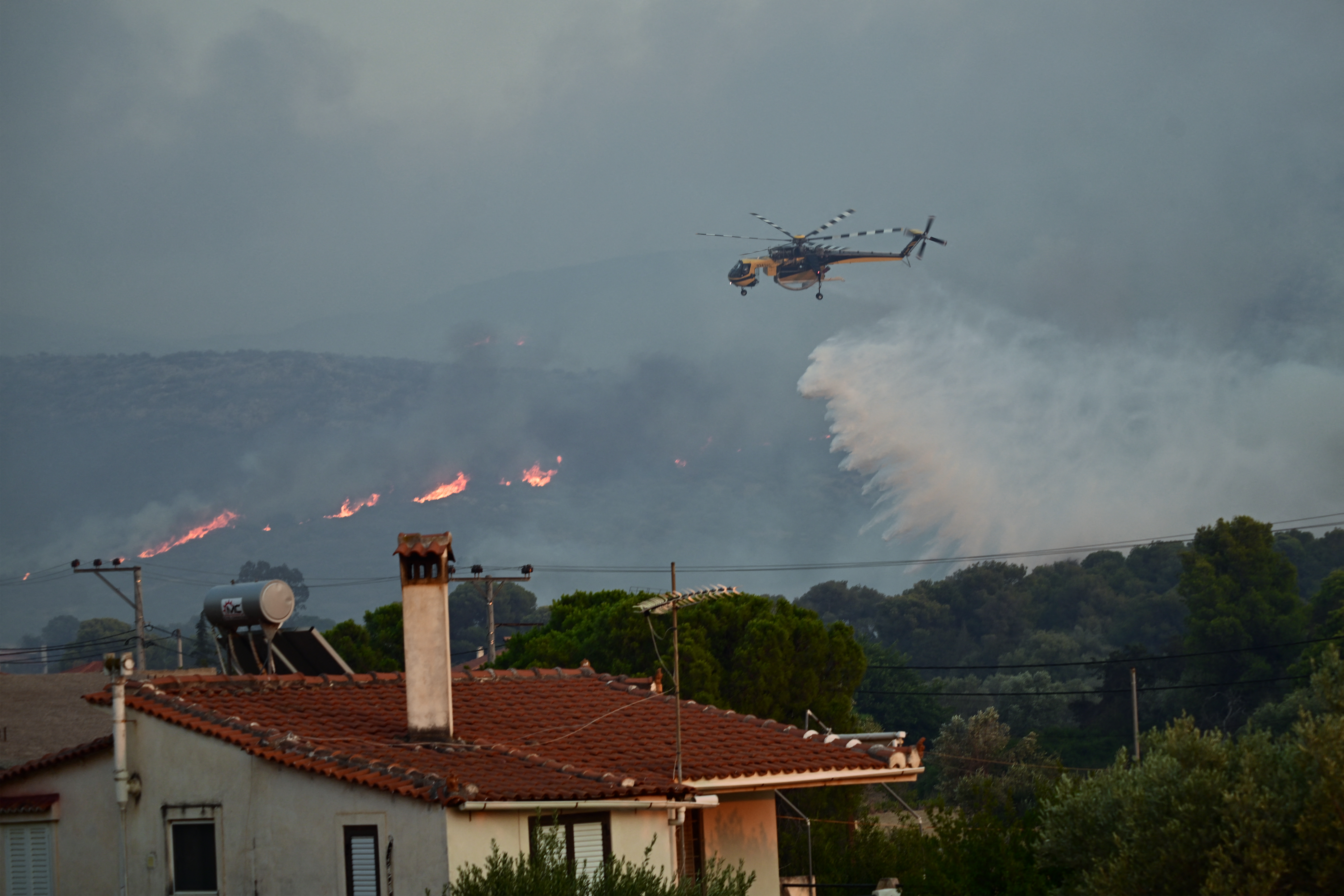 A Sikorsky S-64 Skycrane helicopter drops water over a wildfire as firemen work to extinguish in Palaia Fokaia, some 45 Km south of Athens, on August 8, 2025. (Photo by Aris MESSINIS / AFP)