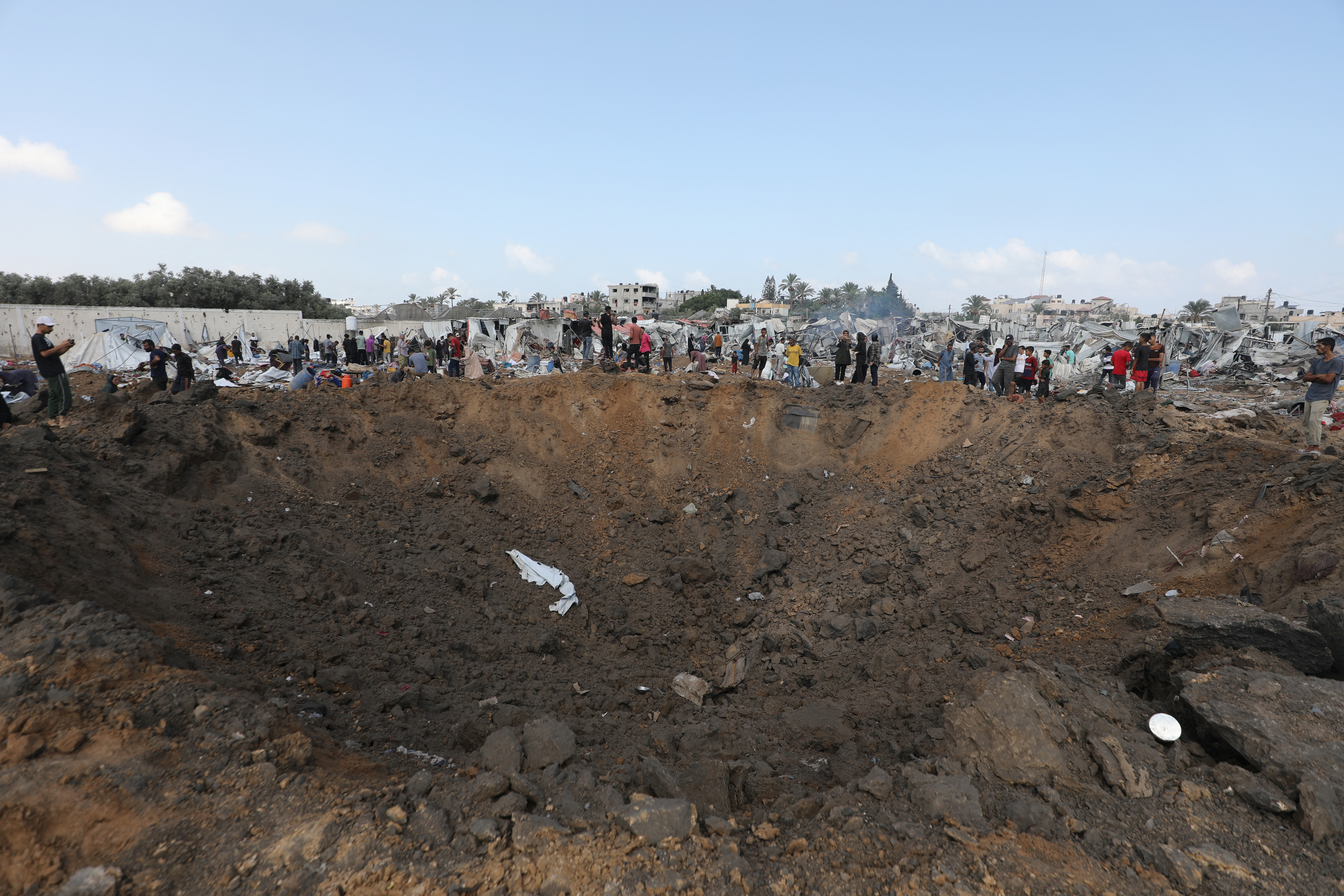 Displaced Palestinians gather around an impact crater left behind after an Israeli strike in Deir el-Balah in Gaza