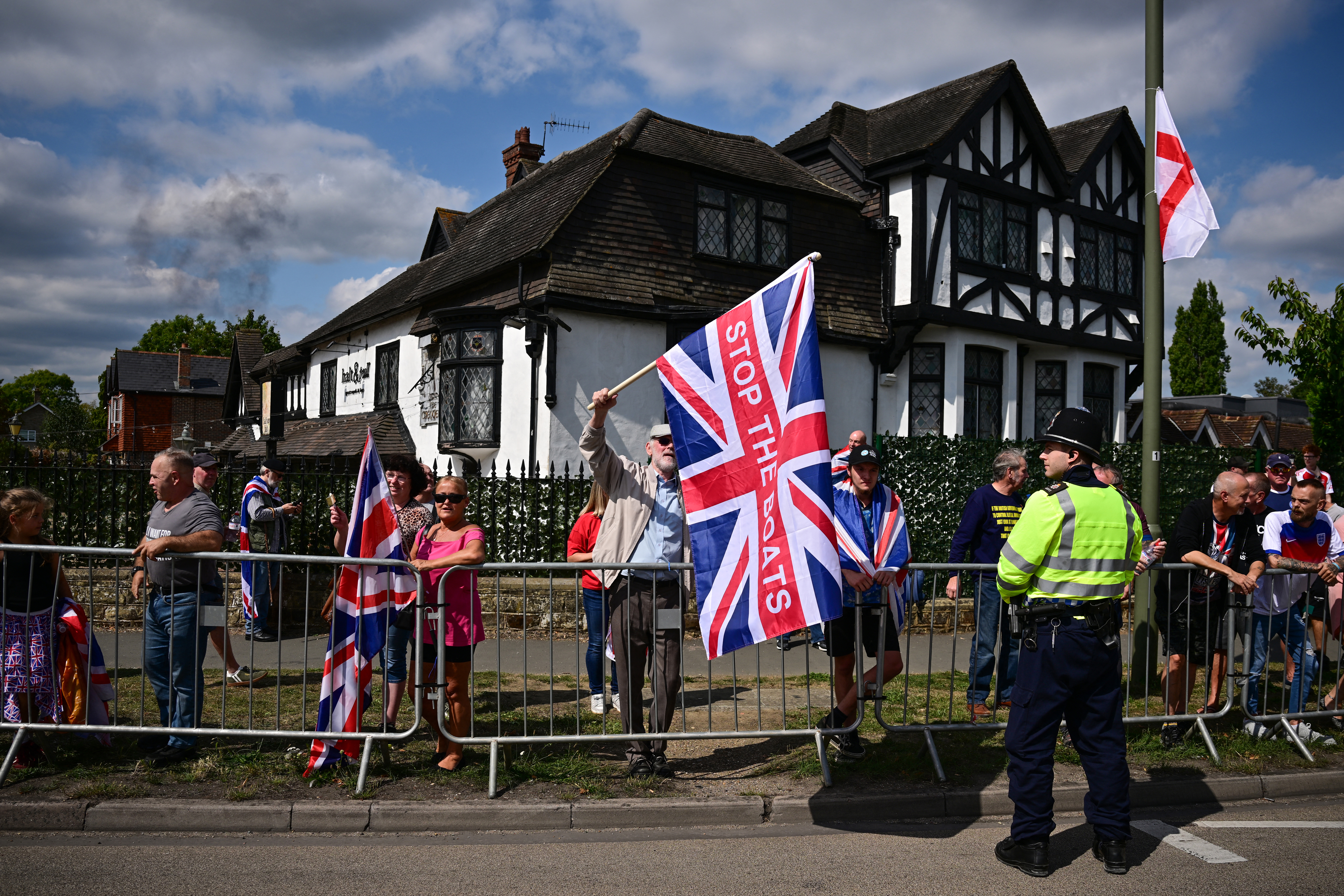 people hold a large British flag at a small protest in a British village