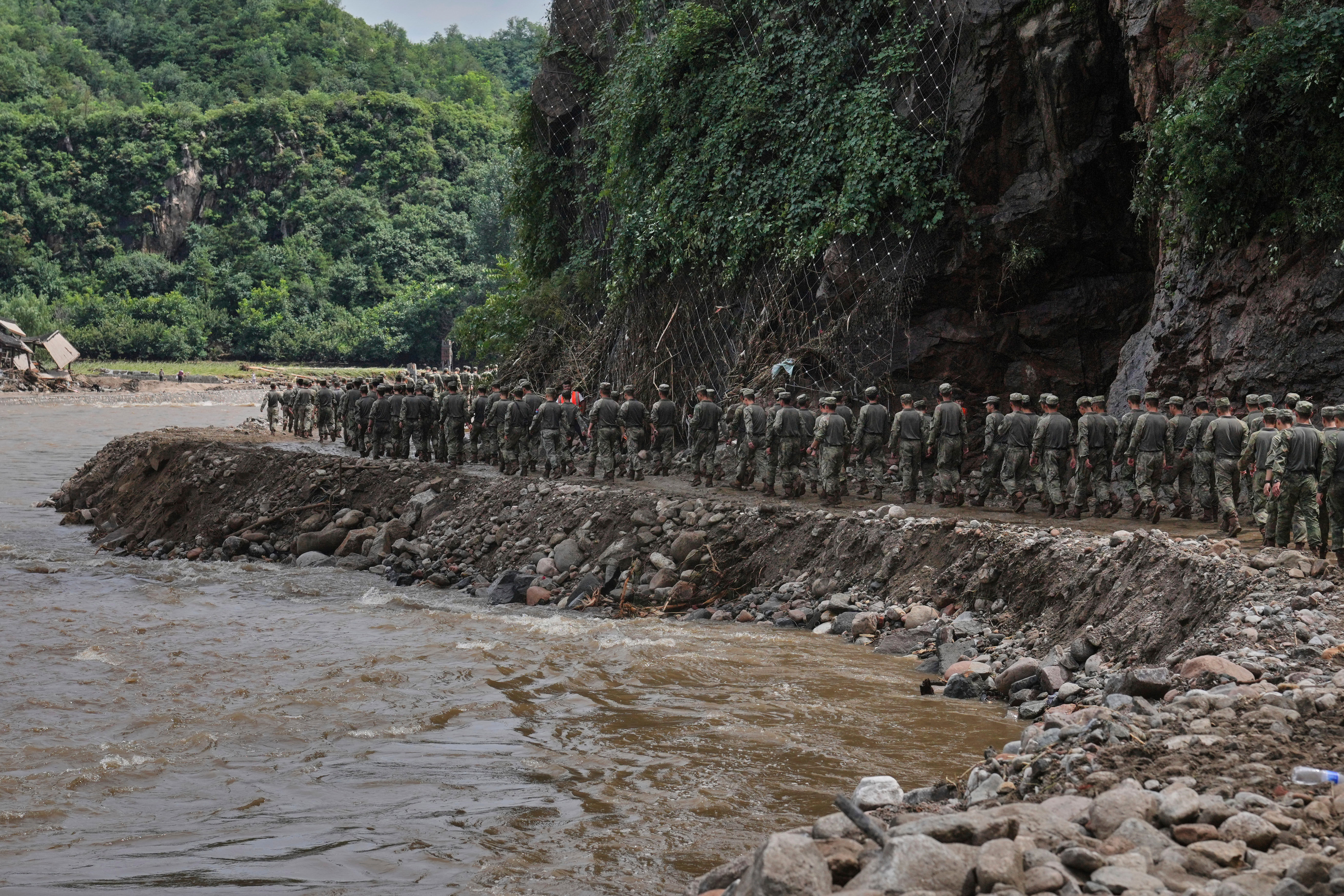 Soldiers march along a road damaged by floods as they head to rescue trapped villagers after heavy rains in Miyun district on the outskirts of Beijing