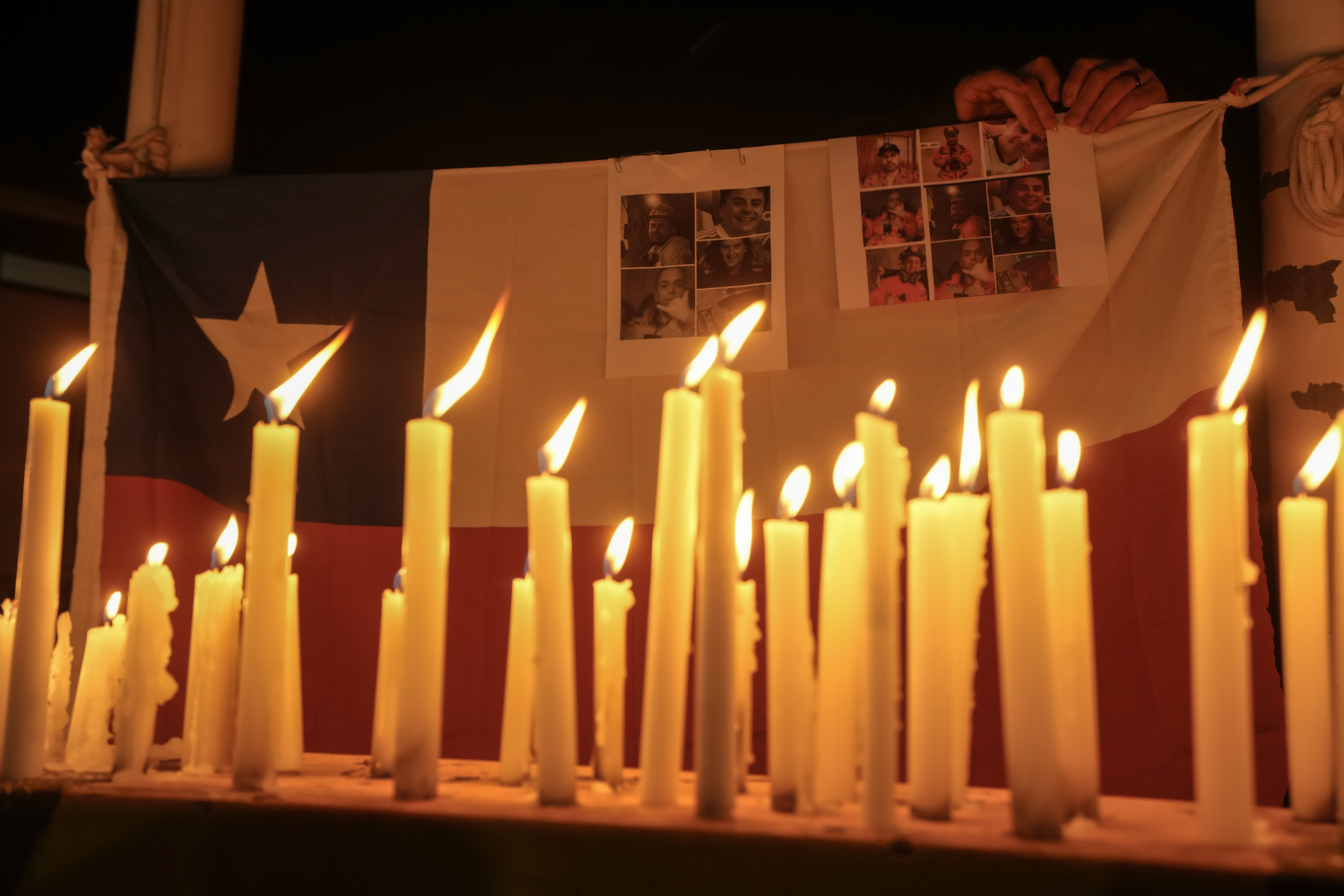 Candles burn during a vigil backdropped with a Chilean national flag and victims of a mine collapse in front of El Teniente copper mine in Rancagua, Chile on August 2, 2025.
