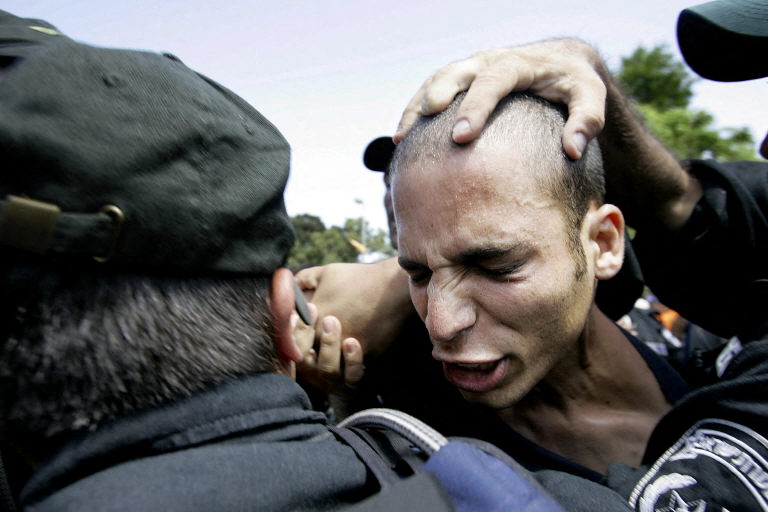 An Israeli settler is arrested by border police as protestors tried to stop the police to make their way up the main street in the southern Gaza Strip settlement of Neveh Dekalim early 16 August 2005. Over a dozen settlers were arrested by police after trying to block the entrance to the settlement. More than 50,000 soldiers and policemen are taking part in the uproot operation of 8,000 settlers from Gaza Strip which started yesterday when the Israeli government gave a 48 hours eviction notice to the settlers; otherwise they will be evacuated by force starting August 17.. AFP PHOTO/ROBERTO SCHMIDT (Photo by ROBERTO SCHMIDT / AFP)