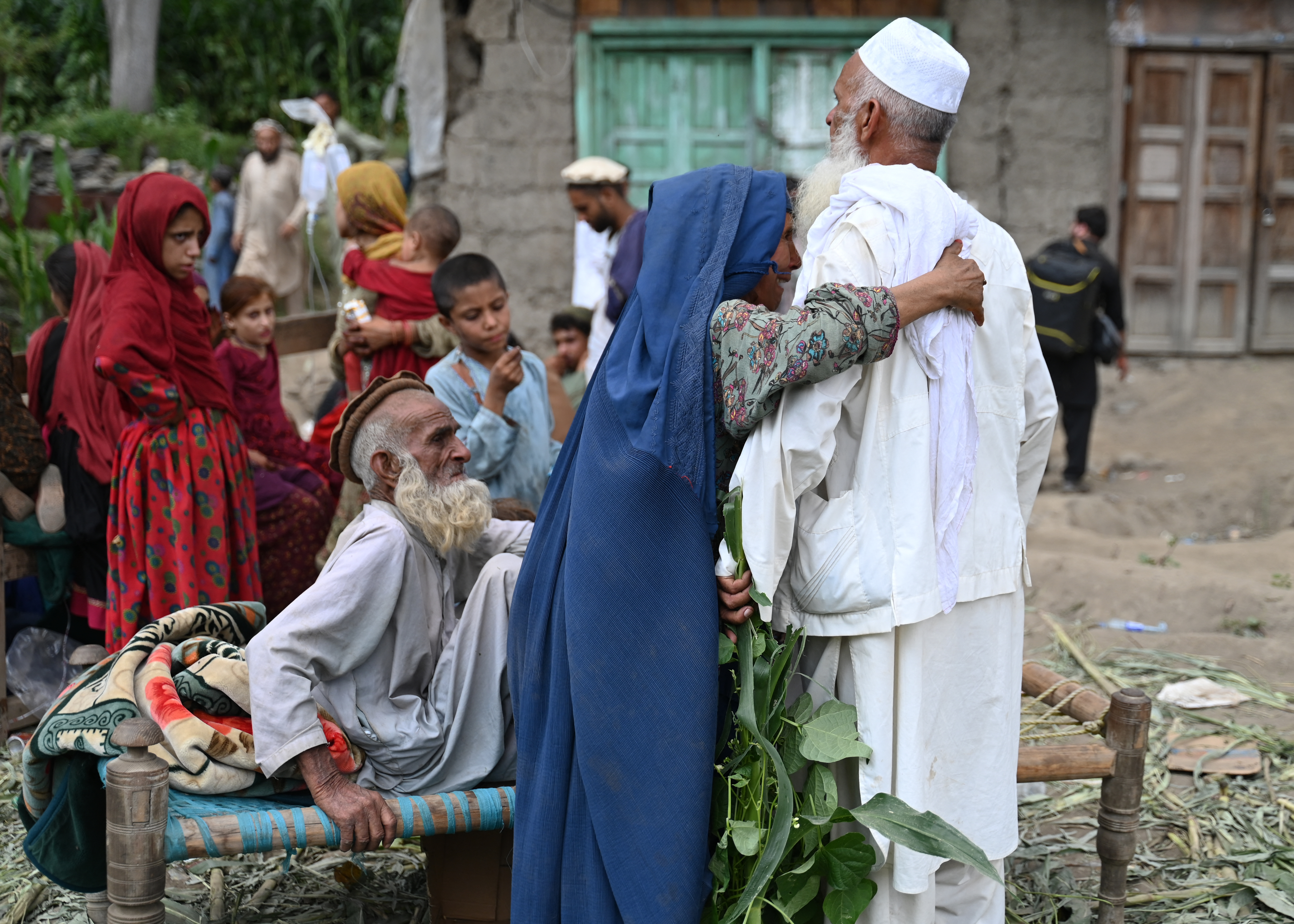 An Afghan woman (C) hugs a man outside a damaged house in the Mazar Dara village of Nurgal, a district of the Kunar Province, in Eastern Afghanistan, on September 1, 2025.