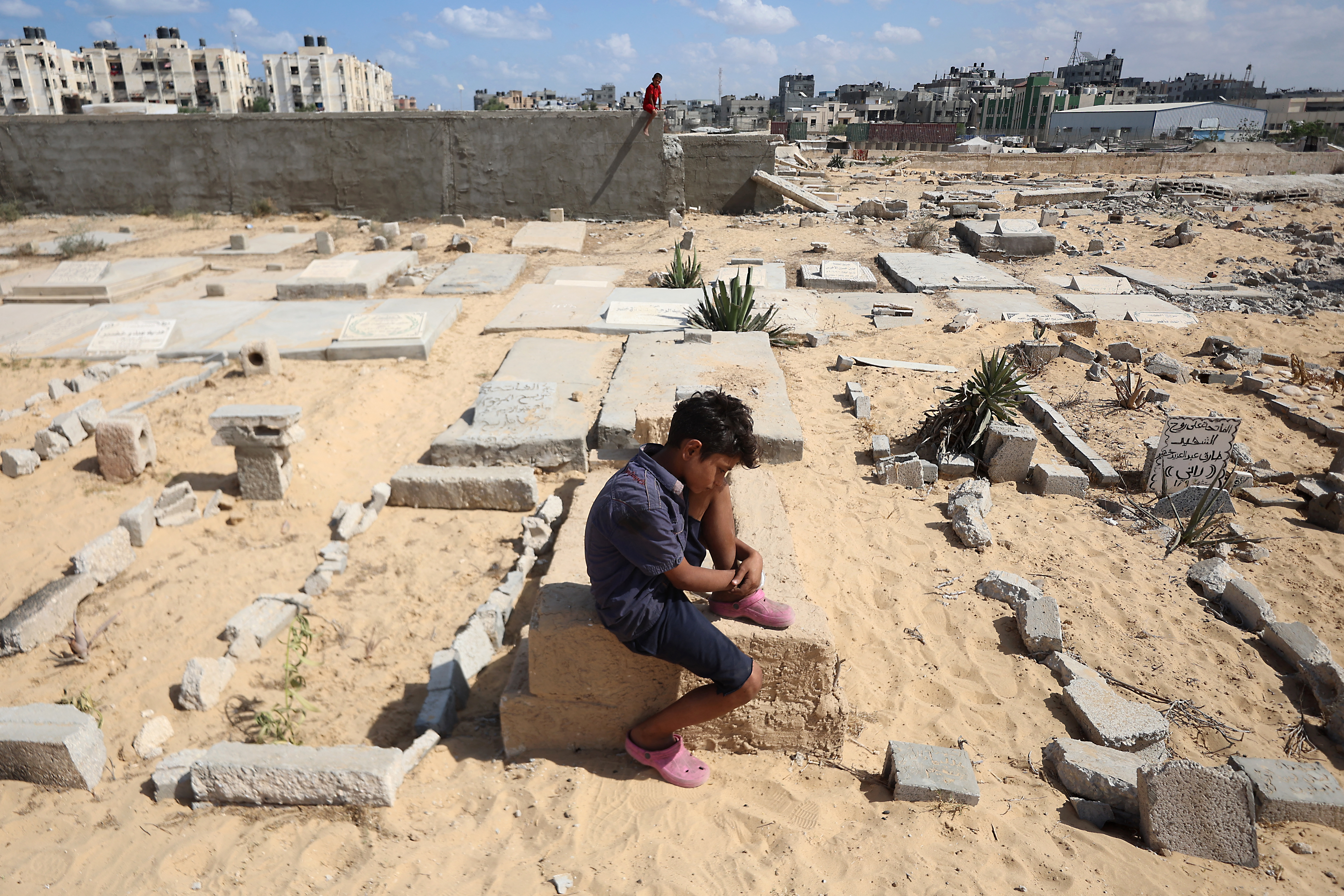 A boy sits on top of a tomb as displaced Palestinians set up temporary camp in the grounds of a cemetary in Khan Yunis in the southern Gaza Strip, on September 25, 2025, amid the ongoing conflict between Israel and the Palestinian militant group Hamas.