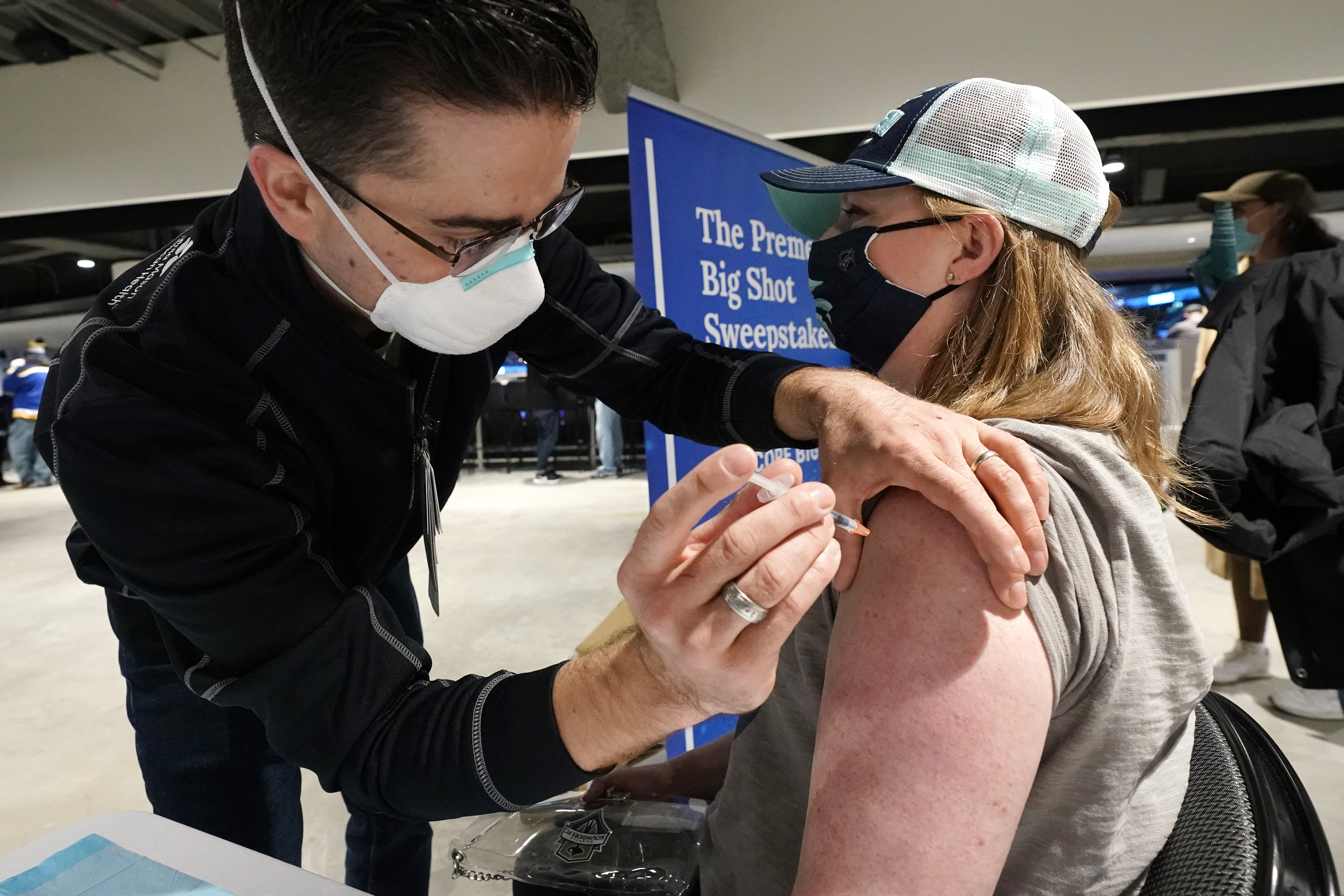 FILE - Seattle Kraken fan Jami Lopez, right, of Bellevue, Wash., receives a Moderna coronavirus booster vaccine from health care worker Zach Hren at the arena before the Kraken's NHL hockey game against the St. Louis Blues, Jan. 21, 2022, in Seattle. (AP Photo/Elaine Thompson, file)