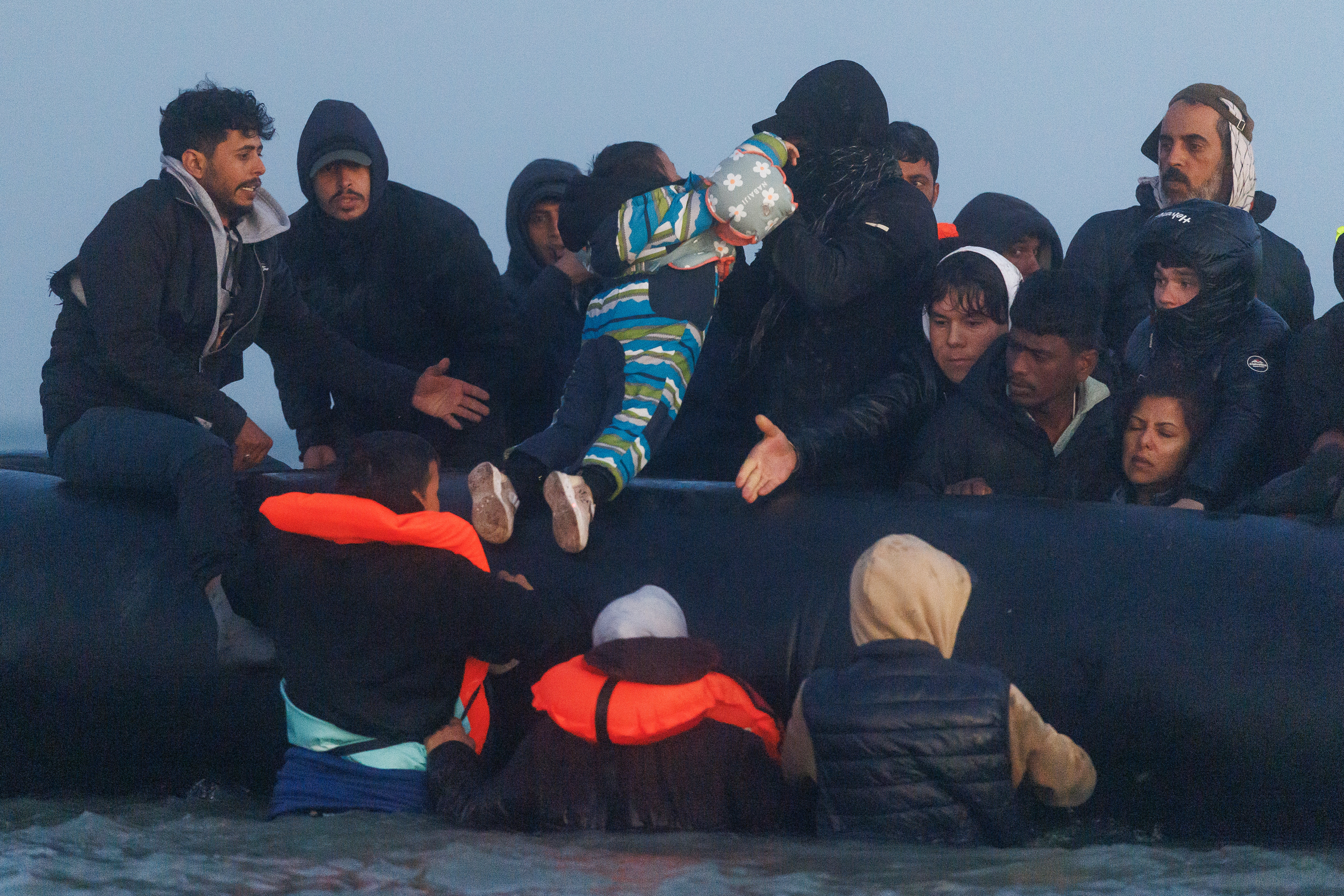 A child is hoisted into a small boat as migrants wait in the water for a 'taxi boat' to take them across the channel to the UK