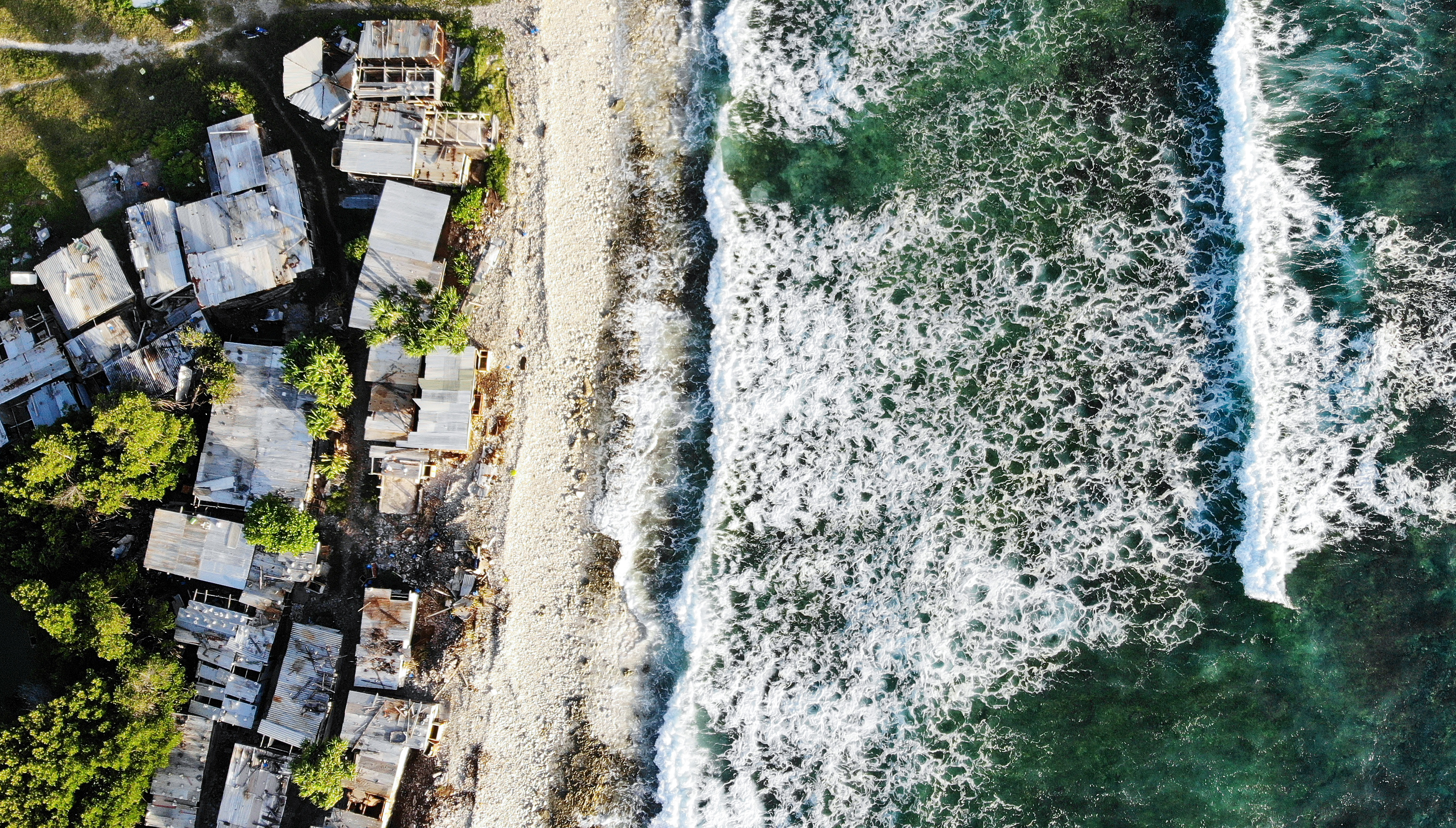 FUNAFUTI, TUVALU - NOVEMBER 28: An aerial view of homes next to the Pacific Ocean on November 28, 2019 in Funafuti, Tuvalu. The low-lying South Pacific island nation of about 11,000 people has been classified as ‘extremely vulnerable’ to climate change by the United Nations Development Programme. The world’s fourth-smallest country is struggling to cope with climate change related impacts including five millimeter per year sea level rise (above the global average), tidal and wave driven flooding, storm surges, rising temperatures, saltwater intrusion and coastal erosion on its nine coral atolls and islands, the highest of which rises about 15 feet above sea level. In addition, the severity of cyclones and droughts in the Pacific Island region are forecast to increase due to global warming. Some scientists have predicted that Tuvalu could become inundated and uninhabitable in 50 to 100 years or less if sea level rise continues. The country is working toward a goal of 100 percent renewable power generation by 2025 in an effort to curb pollution and set an example for larger nations. Tuvalu is also exploring a plan to build an artificial island. (Photo by Mario Tama/Getty Images)