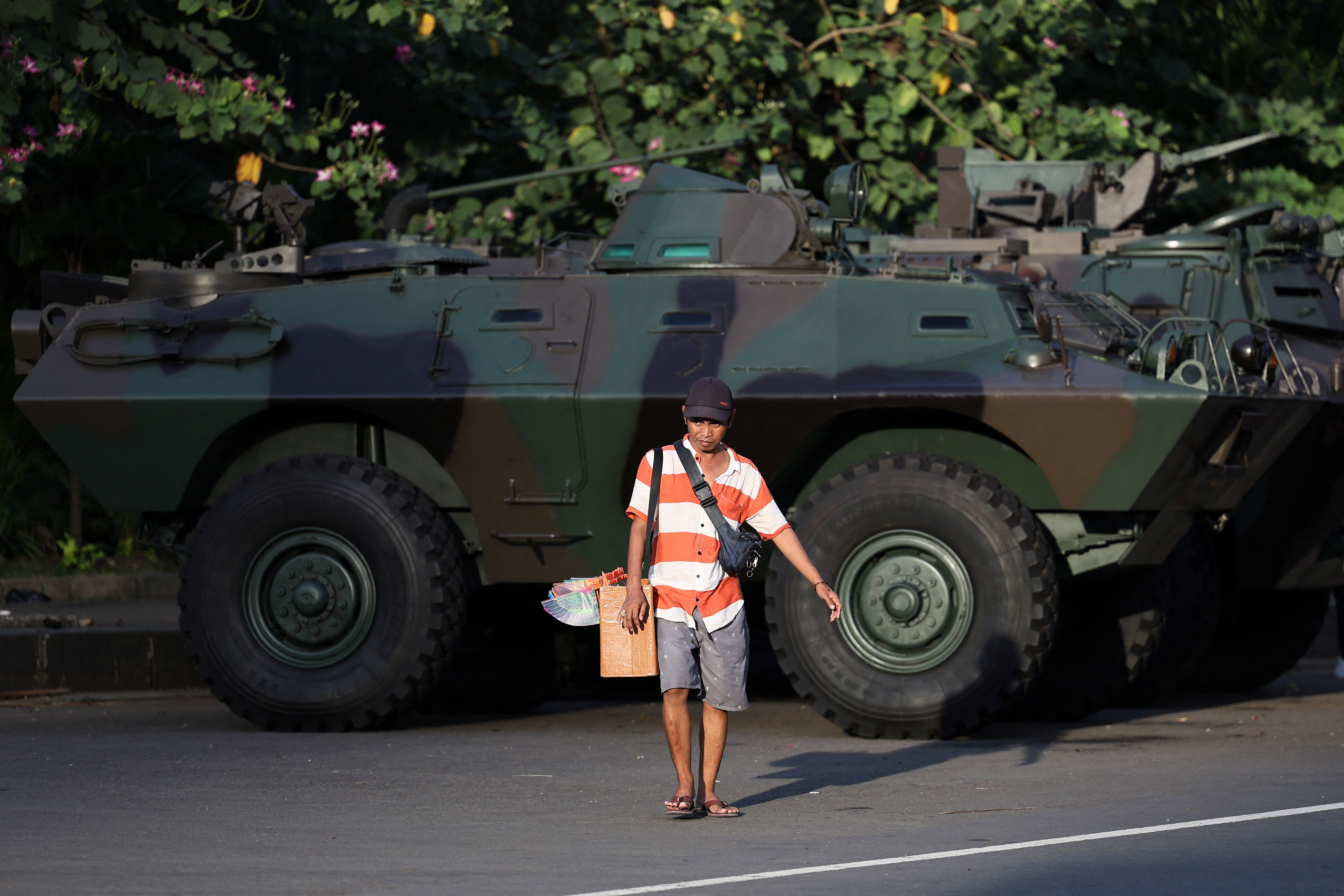 A street vendor walks near an armoured military vehicle.