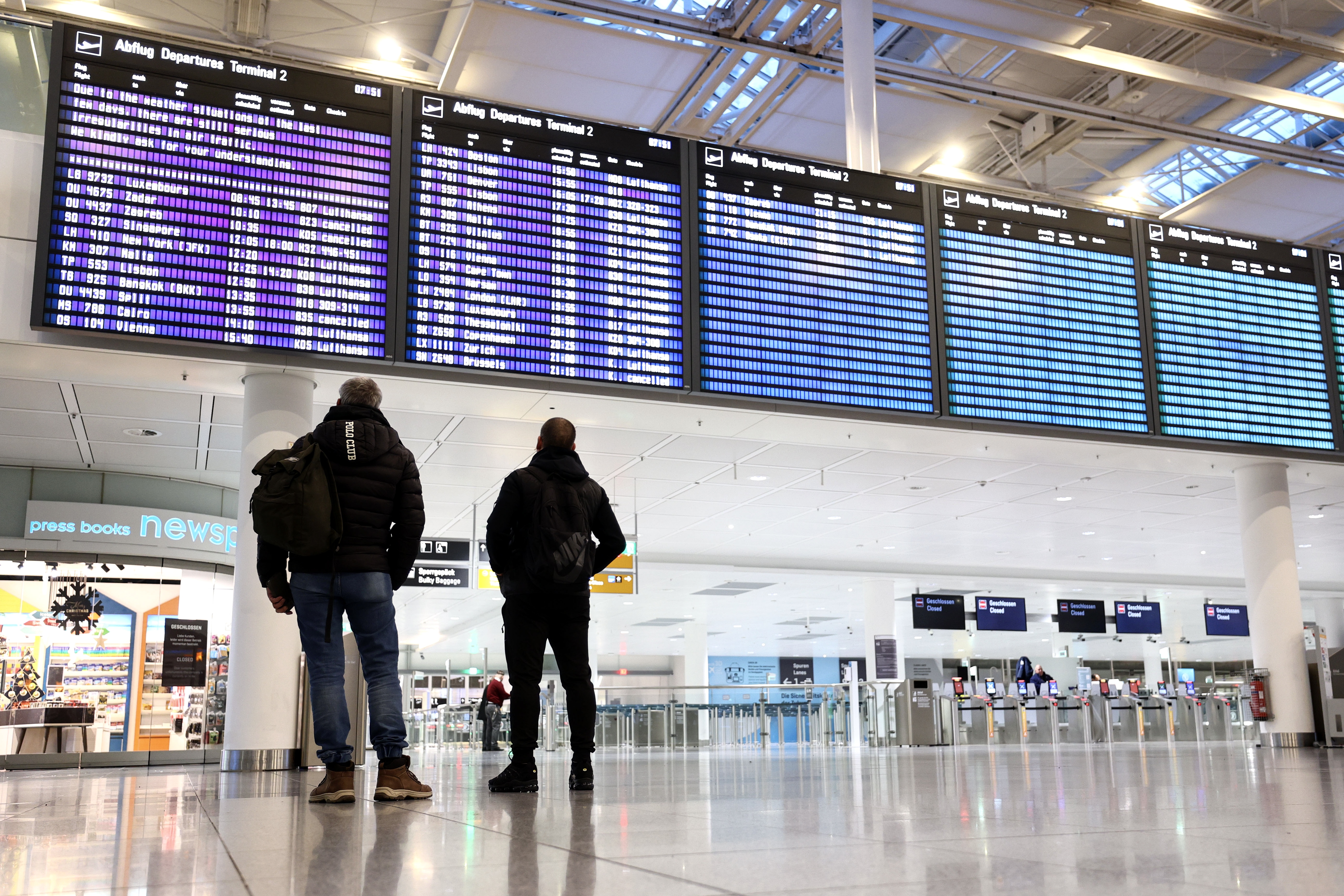 epa11011465 People look at a board announcing irregularities in air traffic at the Munich Airport due to winter weather conditions in Munich, Germany, 05 December 2023. Munich Airport's spokesman announced on the evening of 04 December that there would be no take-offs and landings on 05 December from the start of operations at 6 a.m. to 12 p.m, due to the freezing rain forecast. Flight operations at Munich Airport have been temporarily suspended over the weekend due to heavy snowfall. EPA/ANNA SZILAGYI