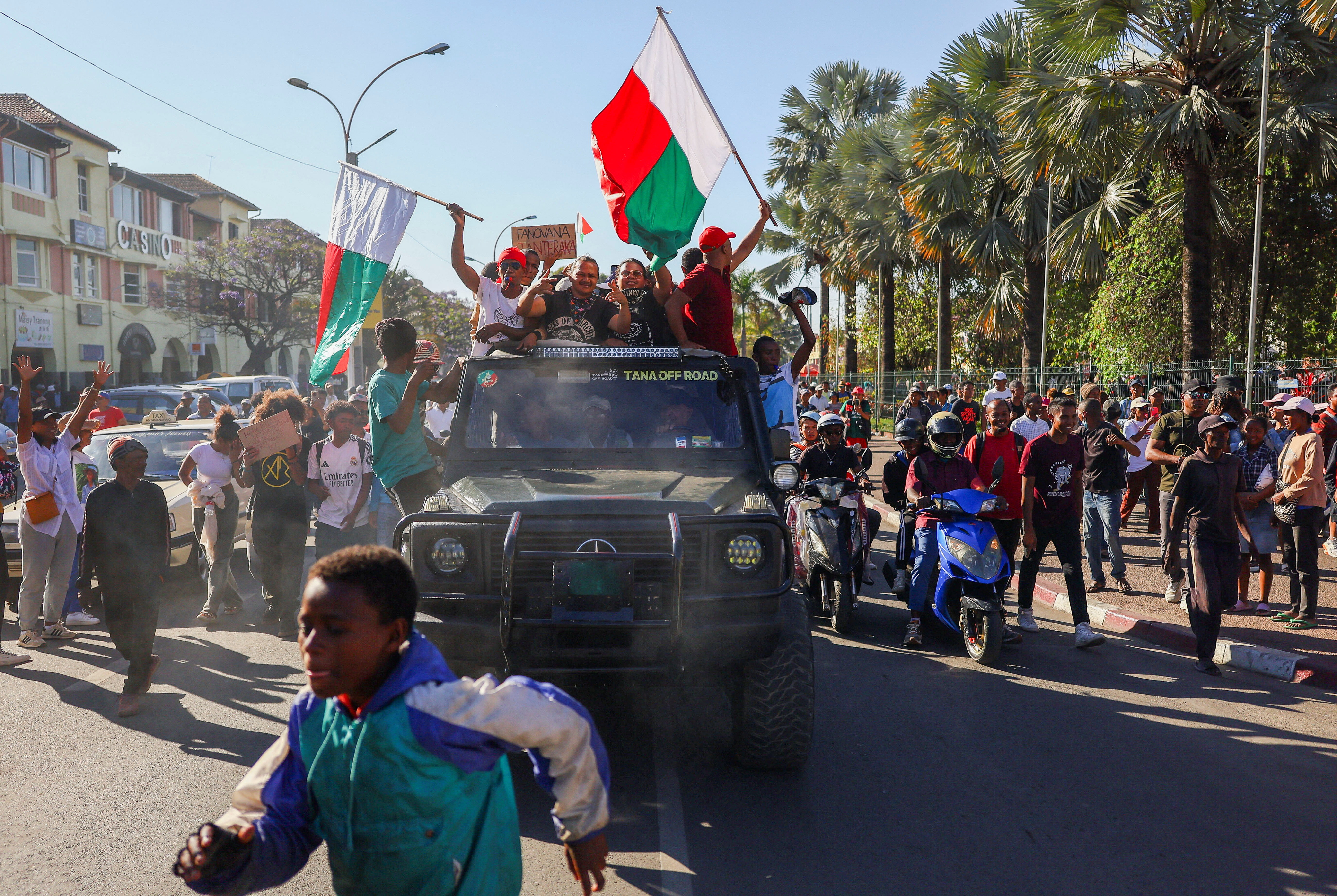 A boy runs past a pick-up truck as people wave flags after the military joined protesters outside the town hall during a youth-led demonstration over power and water shortages, Antananarivo, Madagascar, October 14, 2025 [Siphiwe Sibeko/Reuters]