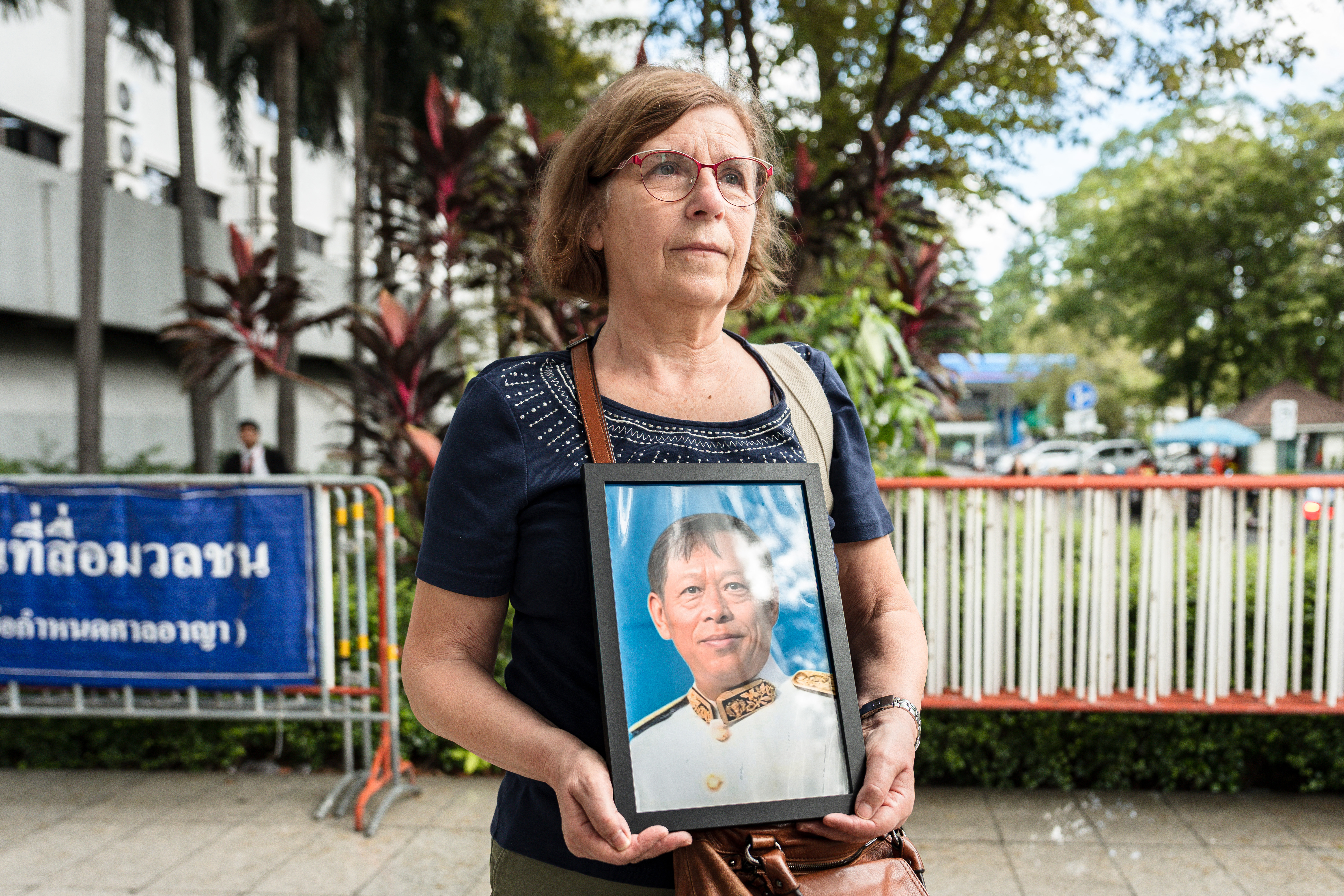 Anne-Marie Lim (C), widow of former Cambodian opposition lawmaker Lim Kimya who was shot dead in Bangkok, holds a picture of her late husband as she arrives at the first witness hearing in the trial at the Criminal Court in Bangkok on September 30, 2025.