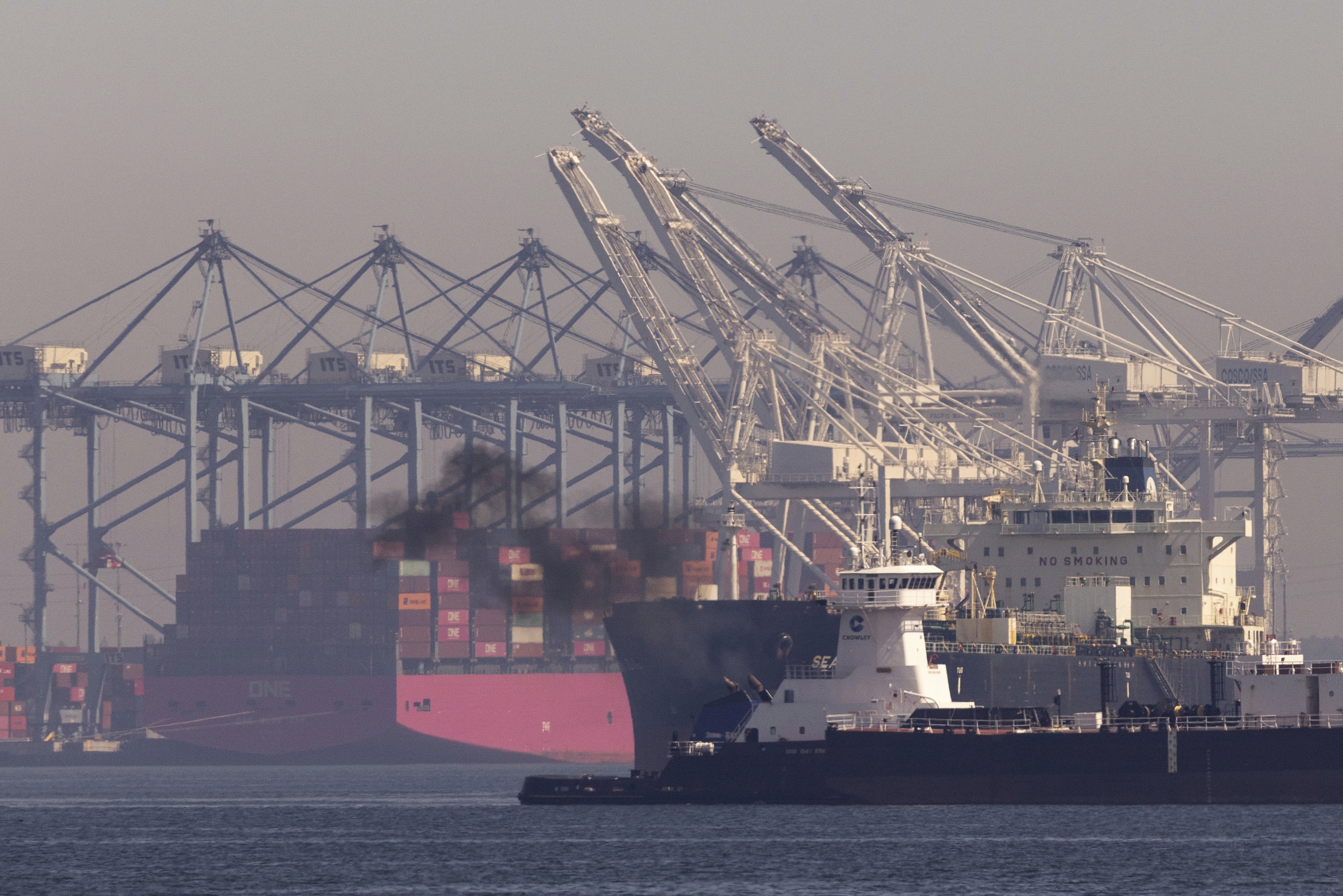 a ship emits a cloud of black smoke in a harbour with grey skies