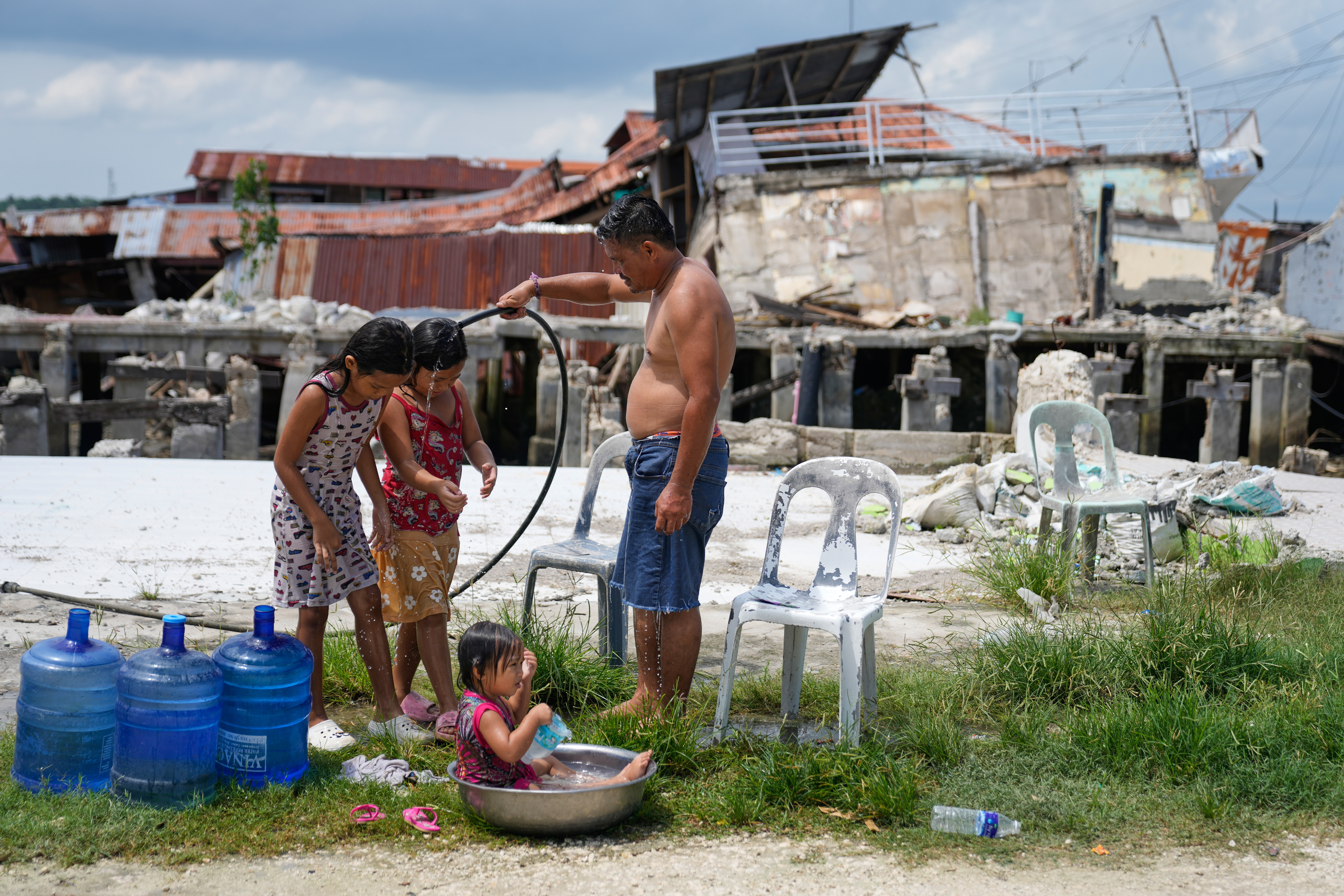 A man takes a bath with his daughters beside damaged structures due to a recent strong earthquake in Bogo, Cebu Province, Central Philippines