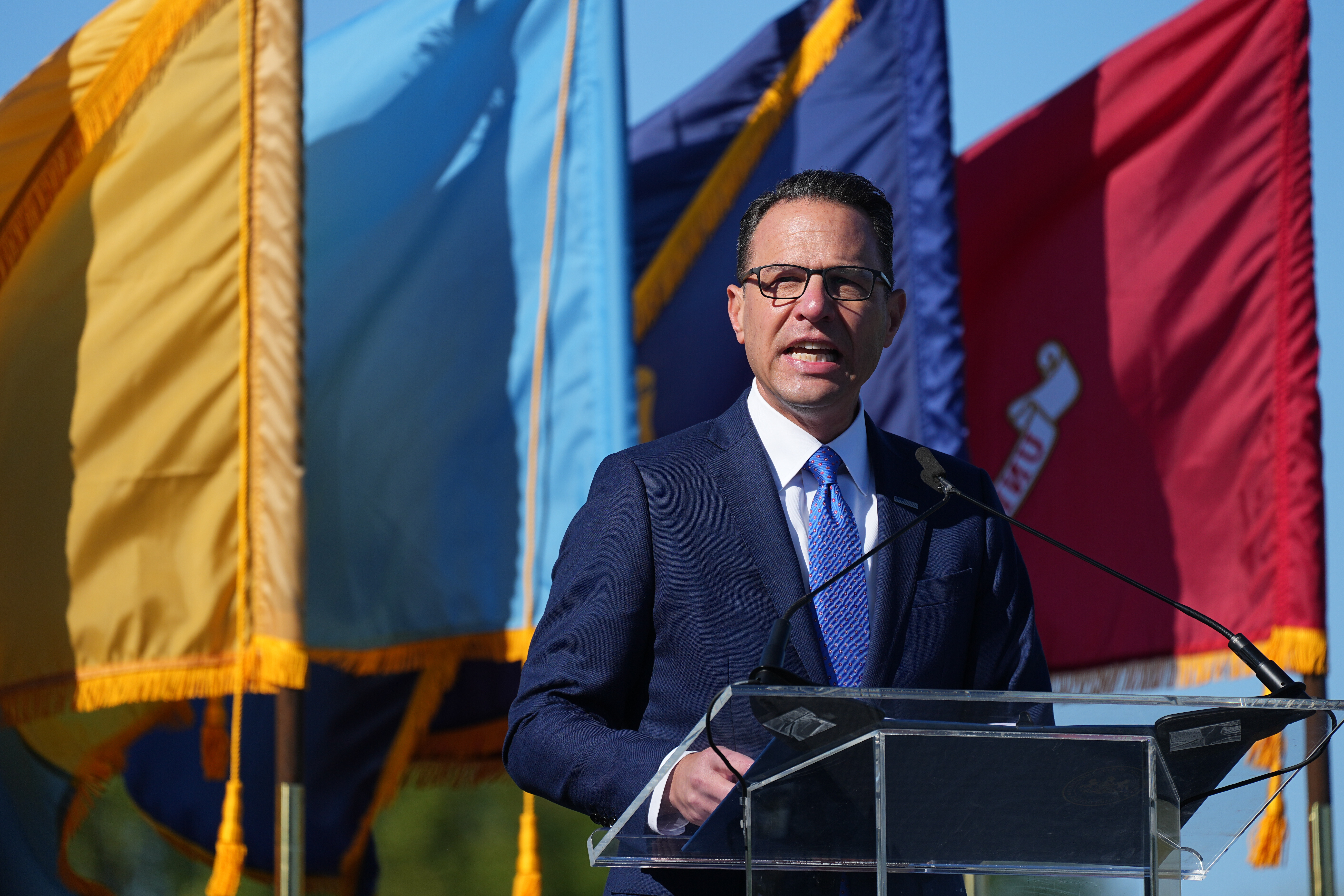 Josh Shapiro speaks at a podium in front of a row of flags.