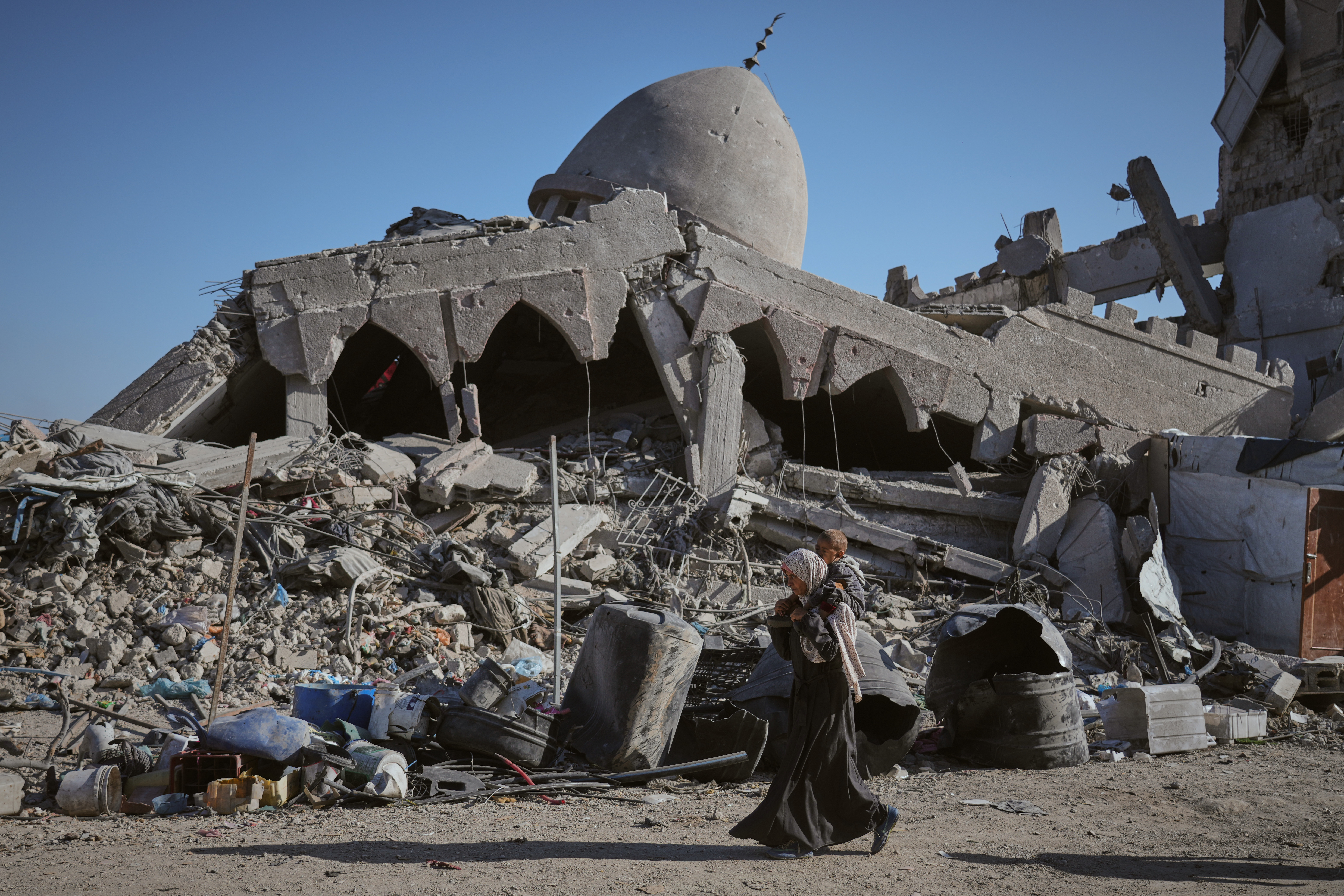 A Palestinian woman carrying her child walks past a destroyed mosque in Gaza City Sunday, Oct. 26, 2025. (AP Photo/Jehad Alshrafi)
