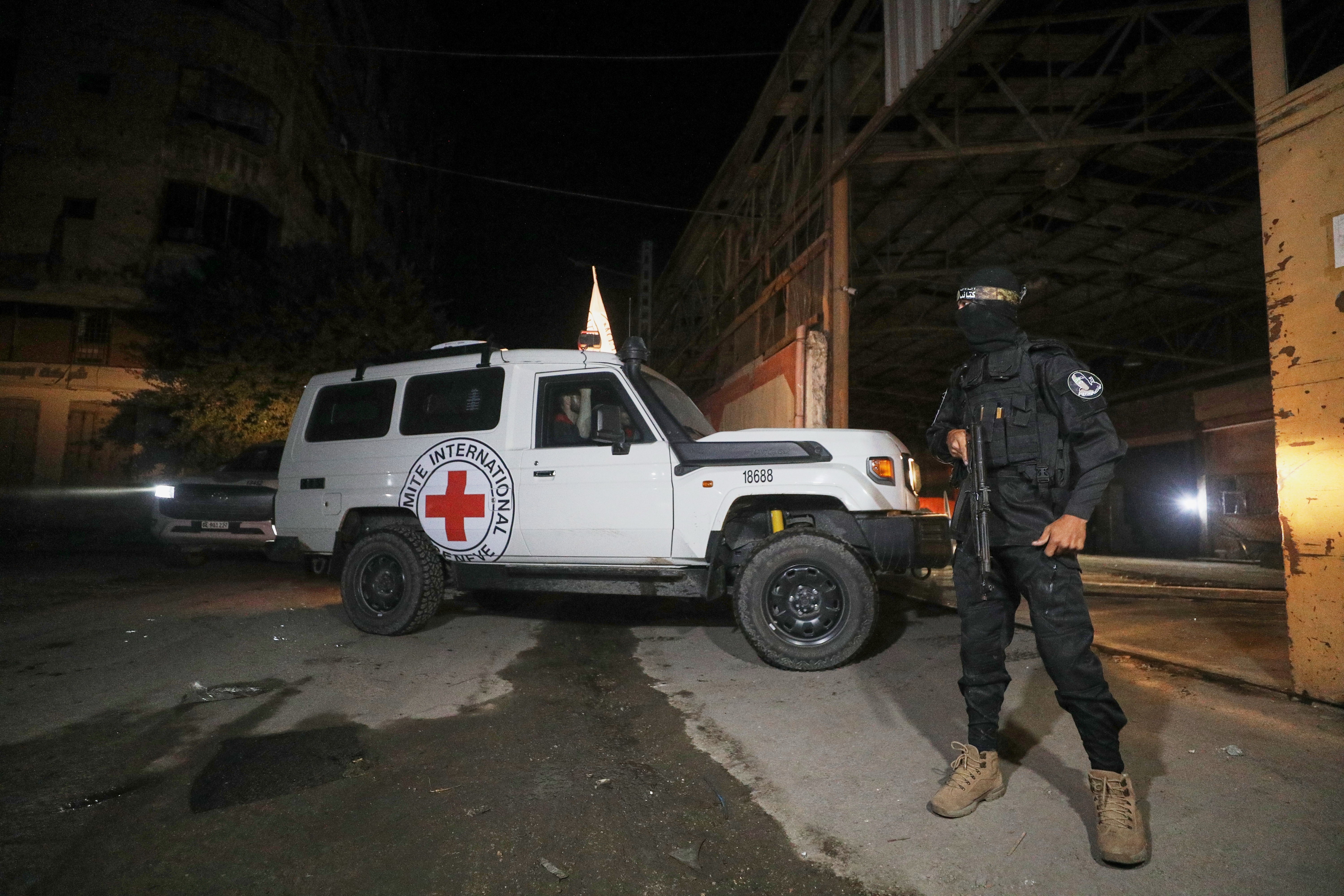 A gunman wearing the uniform of the al-Qassam Brigades, the military wing of Hamas, stands guard as Red Cross vehicles enter a warehouse allegedly to collect coffins containing the bodies of four deceased hostages, in Gaza City, Tuesday, Oct. 14, 2025. (AP Photo/Yousef Al Zanoun)