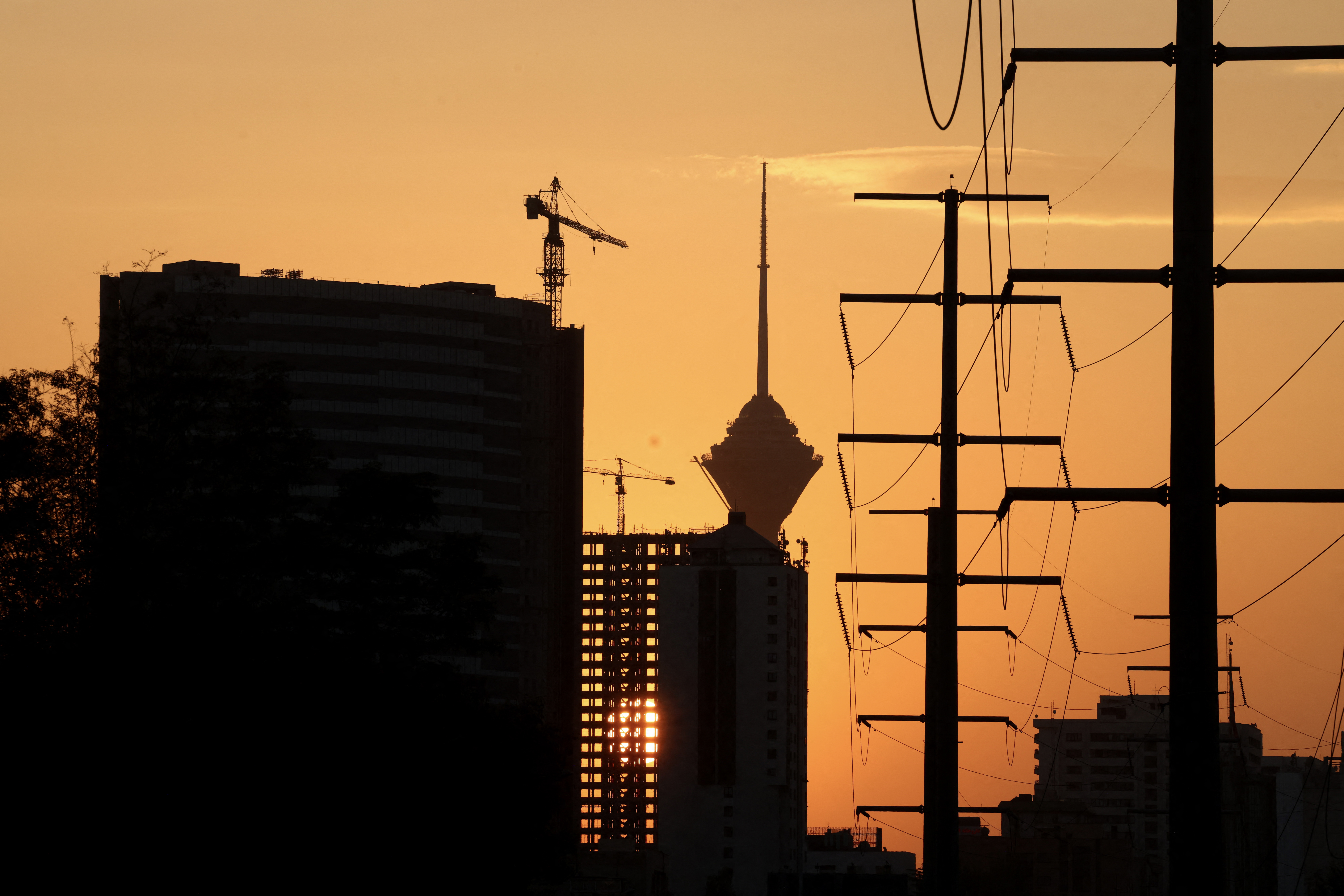 The sun sets behind Milad Telecommunications Tower (C) and a row of electricity pylons in Tehran on October 20, 2025.