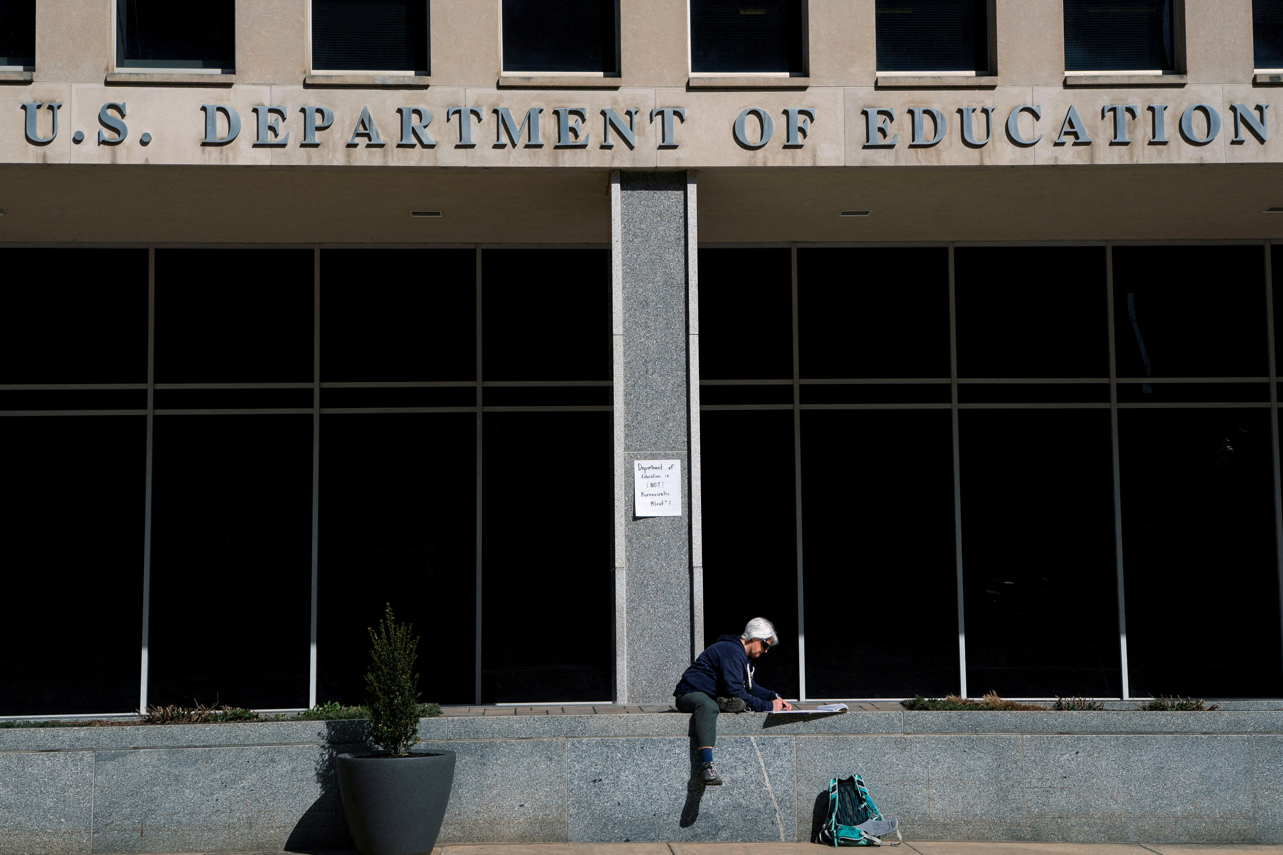 FILE PHOTO: A protester sits near U.S. Department of Education headquarters after the agency said it would lay off nearly half its staff, a possible precursor to closing altogether, as government agencies scrambled to meet President Donald Trump's deadline to submit plans for a second round of mass layoffs, in Washington, D.C., U.S., March 12, 2025. REUTERS/Nathan Howard/File Photo