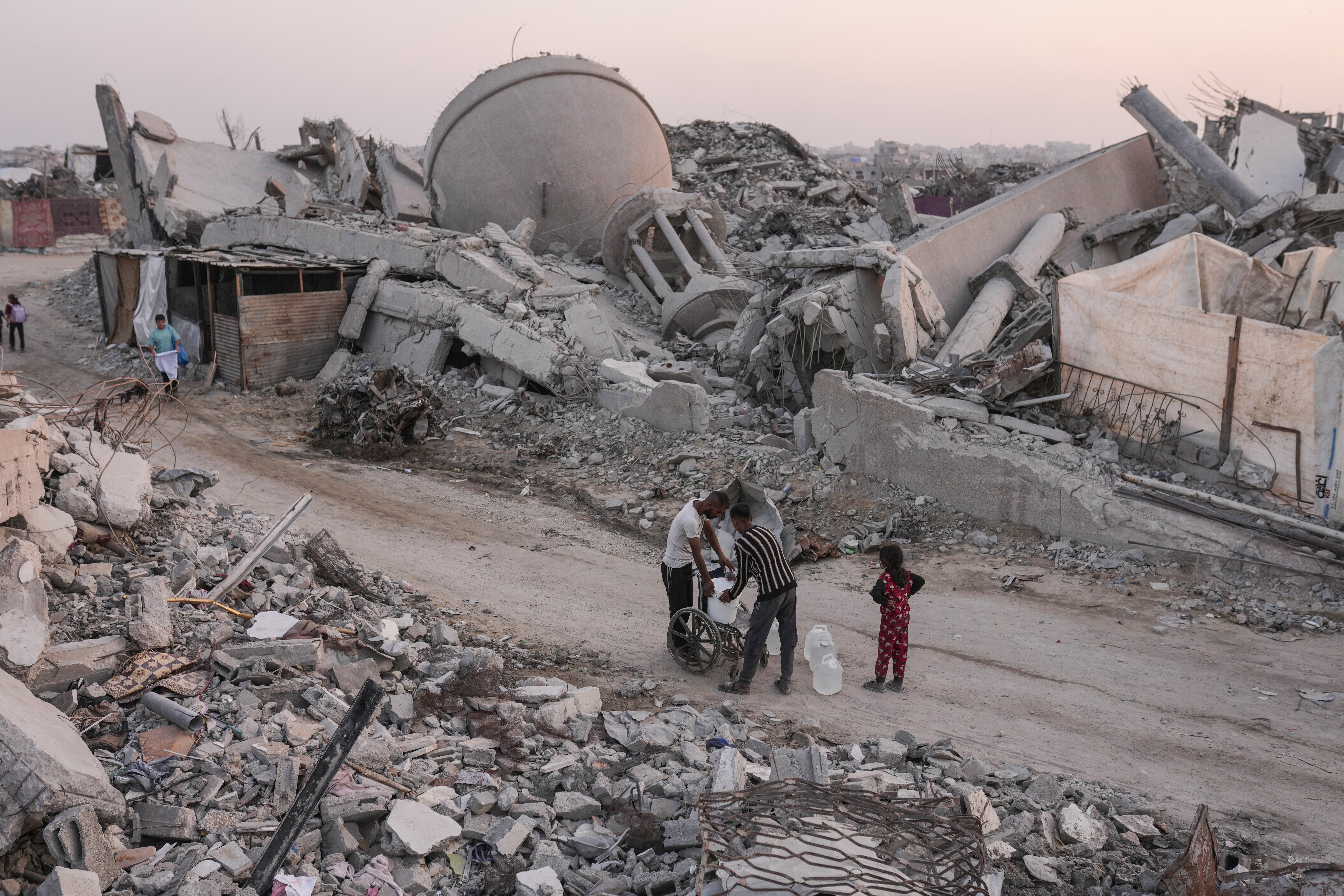 Palestinians carry water through the destruction caused by the Israeli air and ground offensive in the Sheikh Radwan neighbourhood in Gaza City [Jehad Alshrafi/AP Photo]