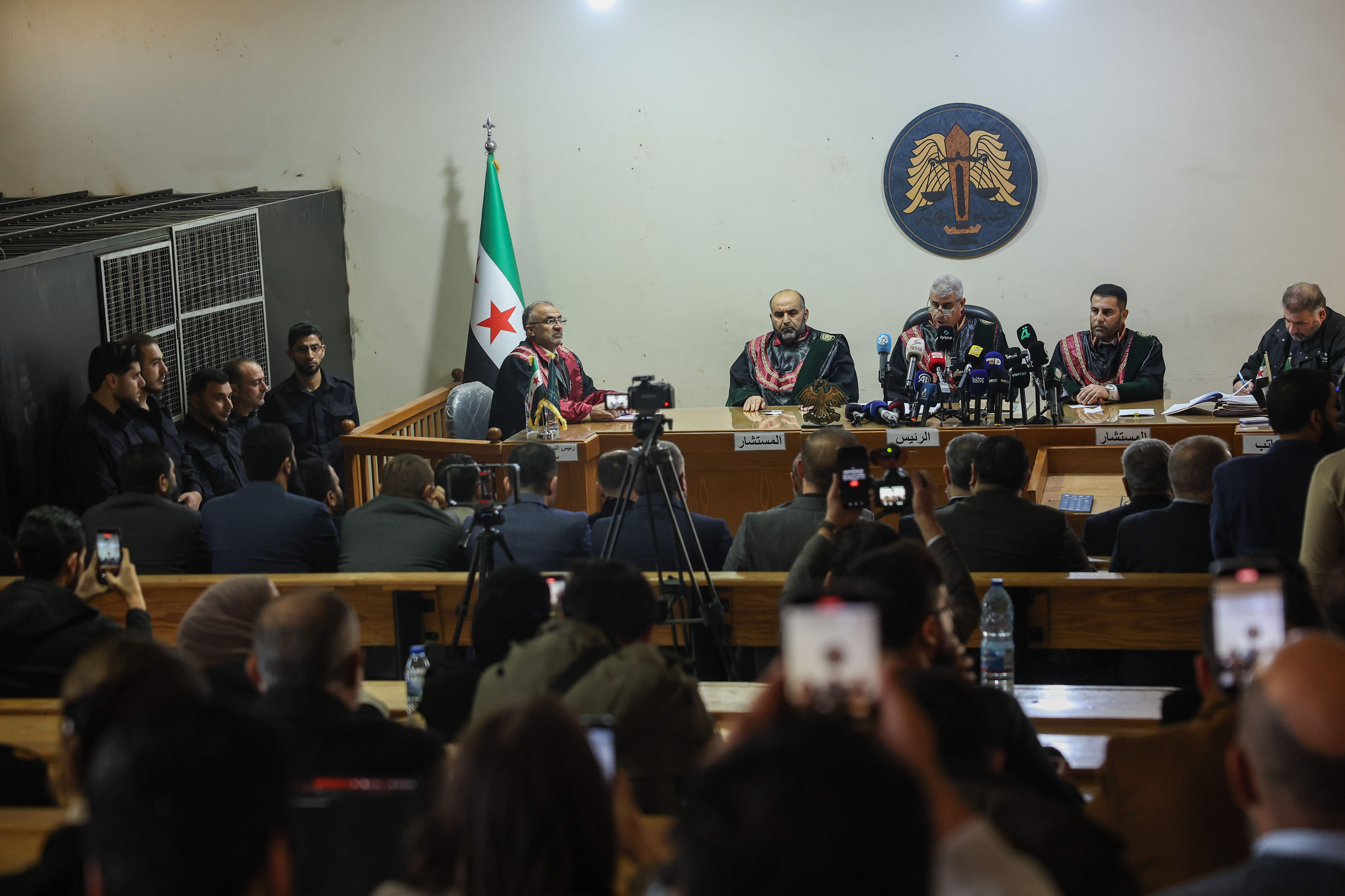 Suspects stand inside a holding cell, left, as judges preside over Syria's first public trial related to deadly clashes in March along the country's coastal provinces, at the Palace of Justice in Aleppo, Syria on November 18, 2025.