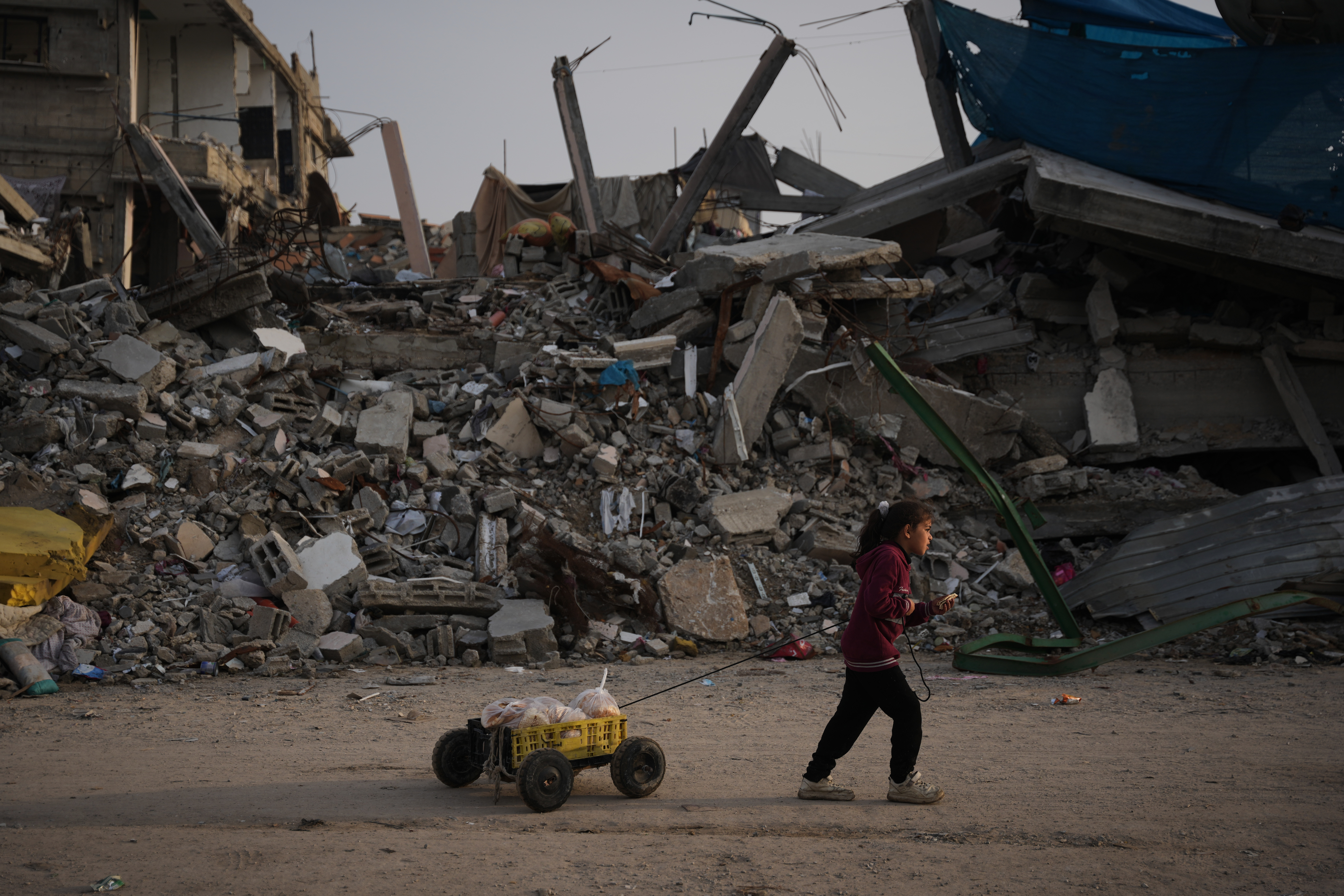 A girl carries bread as she walks past destruction left by Israeli air and ground operations in Gaza City on Saturday, November 29, 2025 [Abdel Kareem Hana/AP]