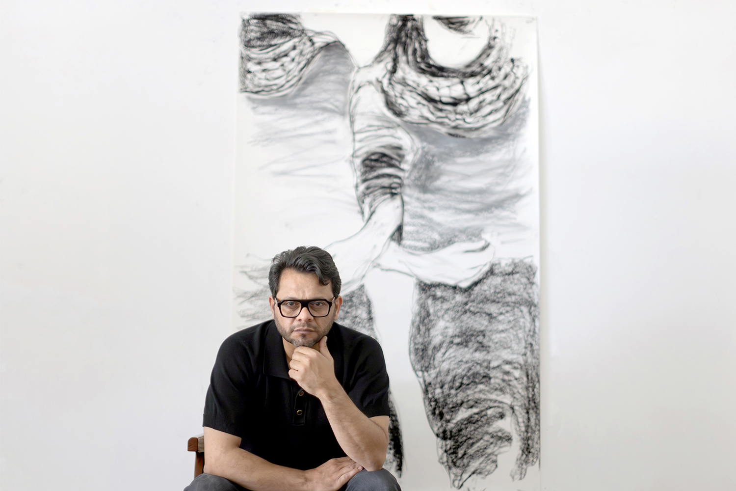 Hazem Harb sits in front of a grayscale artwork, his chin on his hand