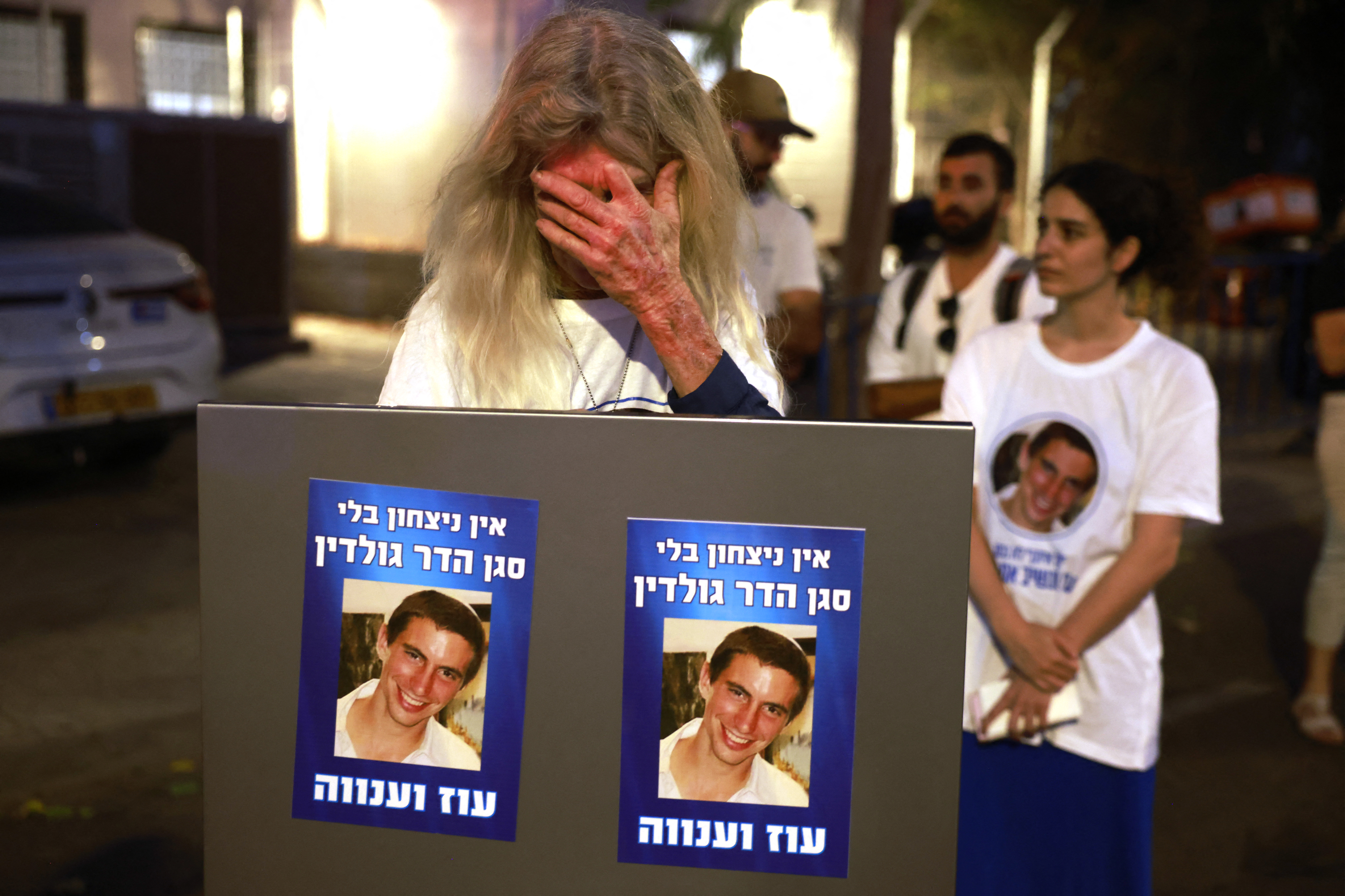 An Israeli woman holding portraits bearing the image of Lt. Hadar Goldin reacts as she waits for the arrival of the body believed to be that of Goldin, whom Hamas claims to have returned as part of a ceasefire agreement between Israel and Palestinian factions in Gaza, outside the National Center for Forensic Medicine in Tel Aviv on November 9, 2025.