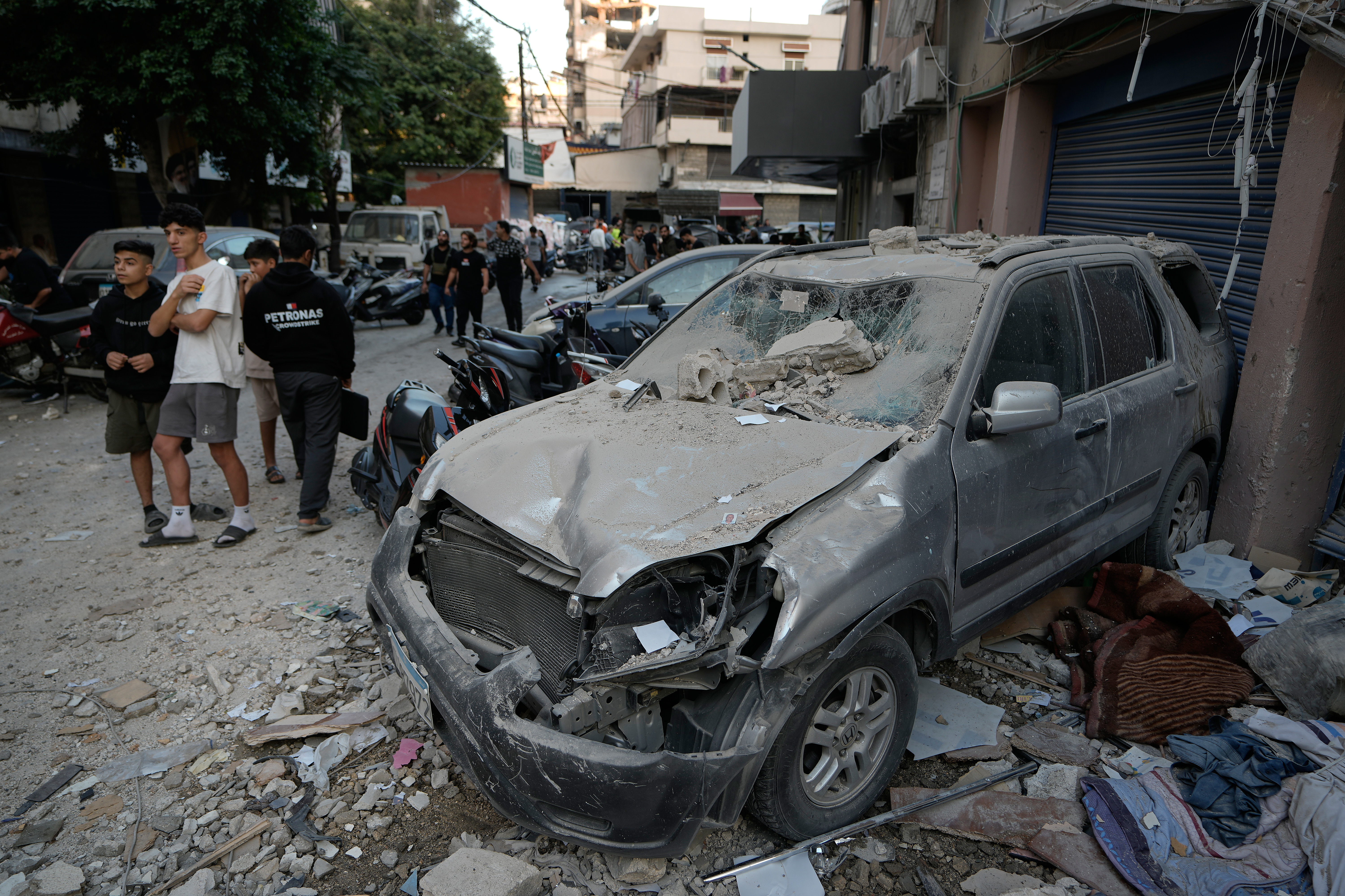 People pass a damaged car at the site where an Israeli strike hit an apartment building on Dahiyeh in the southern suburb of Beirut, Sunday, Nov. 23, 2025. (AP Photo/Bilal Hussein)