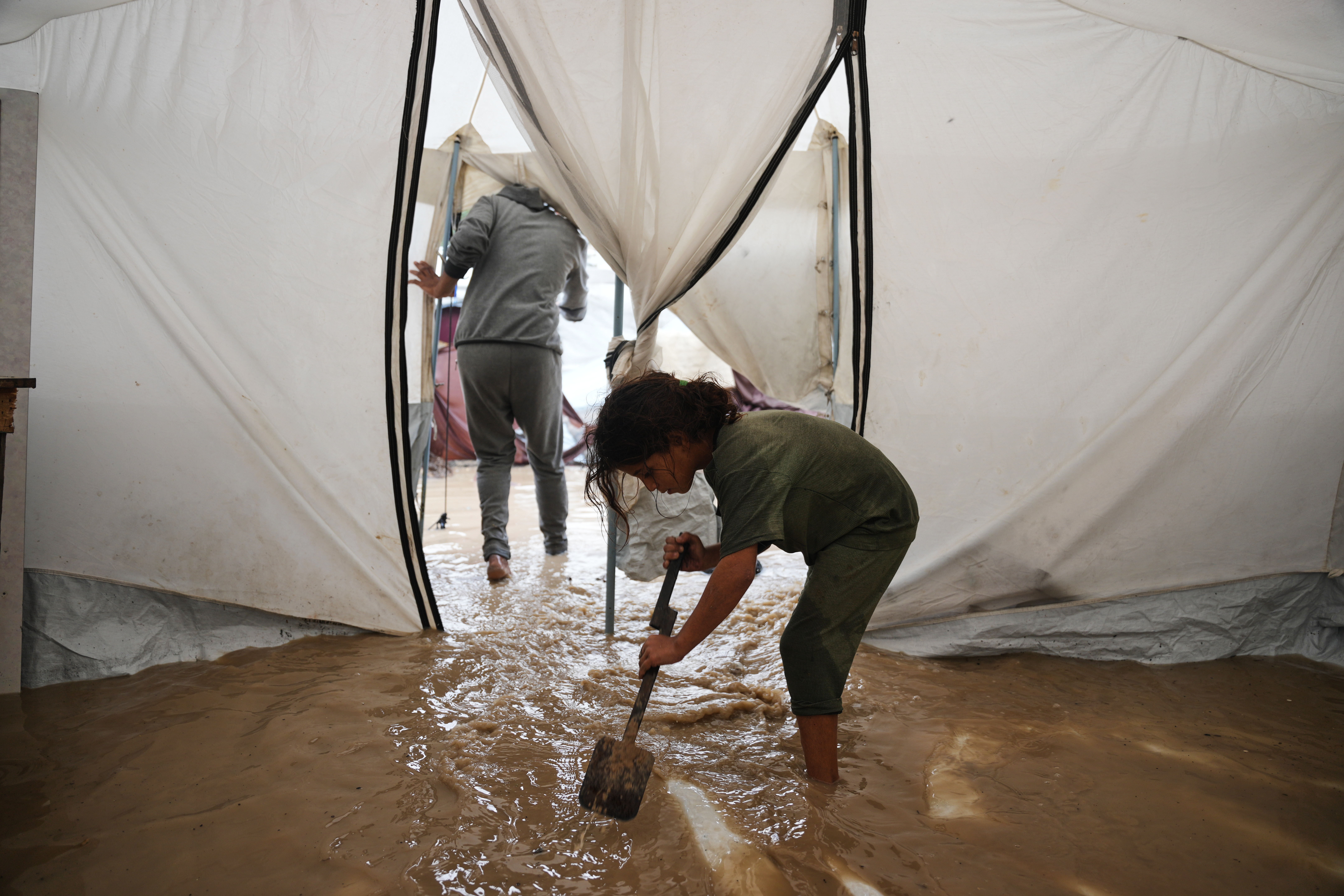 Saja Fayyad, 7, tries to clear water from her family's flooded tent at a temporary camp for displaced Palestinians after heavy rainfall in Deir al-Balah, central Gaza Strip, Tuesday, Nov. 25, 2025. (AP Photo/Abdel Kareem Hana)