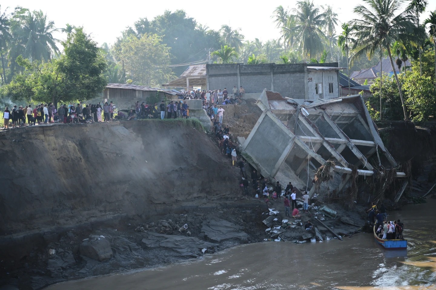 People walk down the embankment of a river to take a boat ride across after a bridge nearby collapsed during a flood.