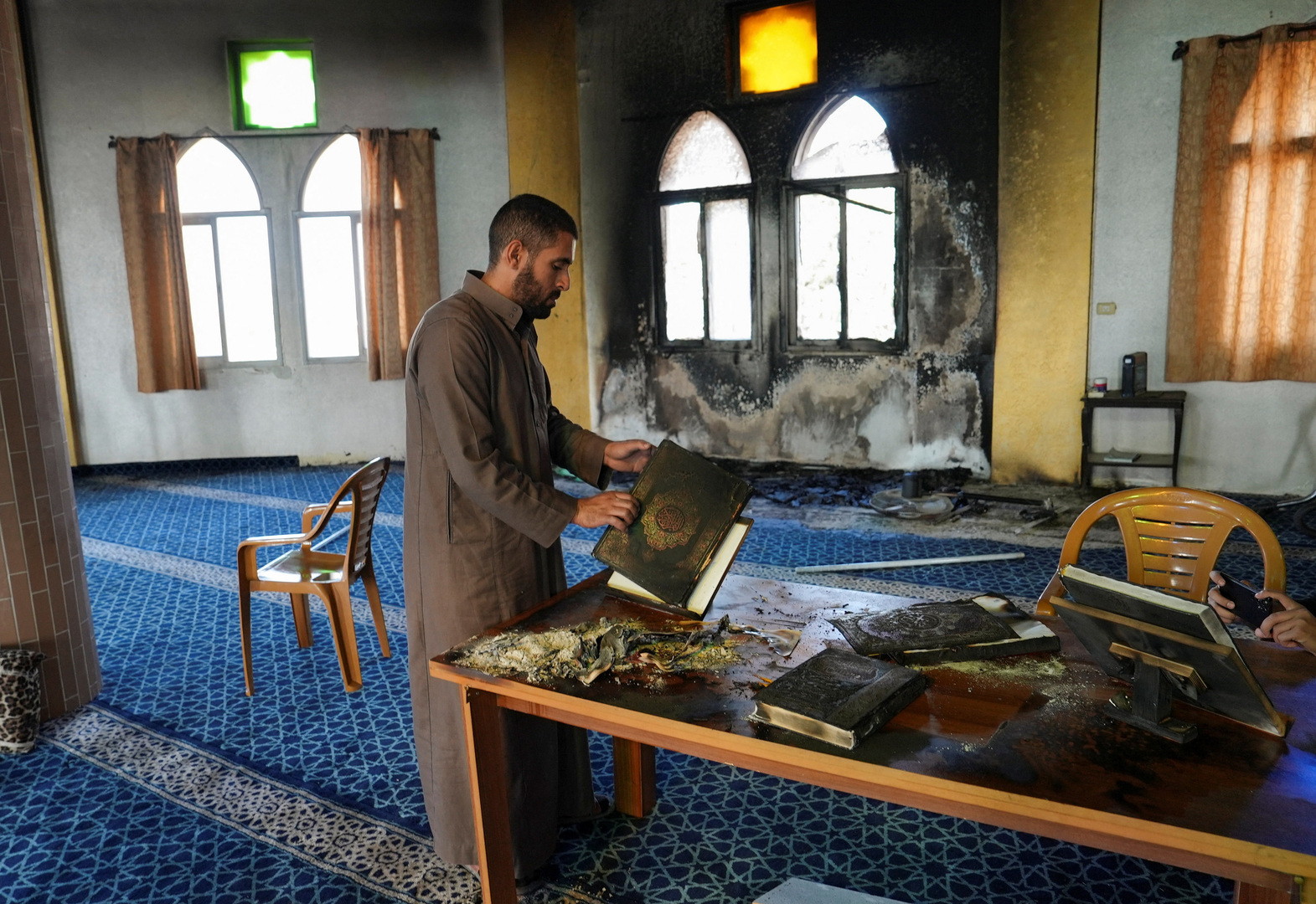 A Palestinian man handles a burned Koran in a mosque, following an attack that local Palestinians said was carried out by Israeli settlers in Deir Istiya village, near Salfit in the Israeli-occupied West Bank on Nov. 13, 2025. [Ali Sawafta/Reuters]