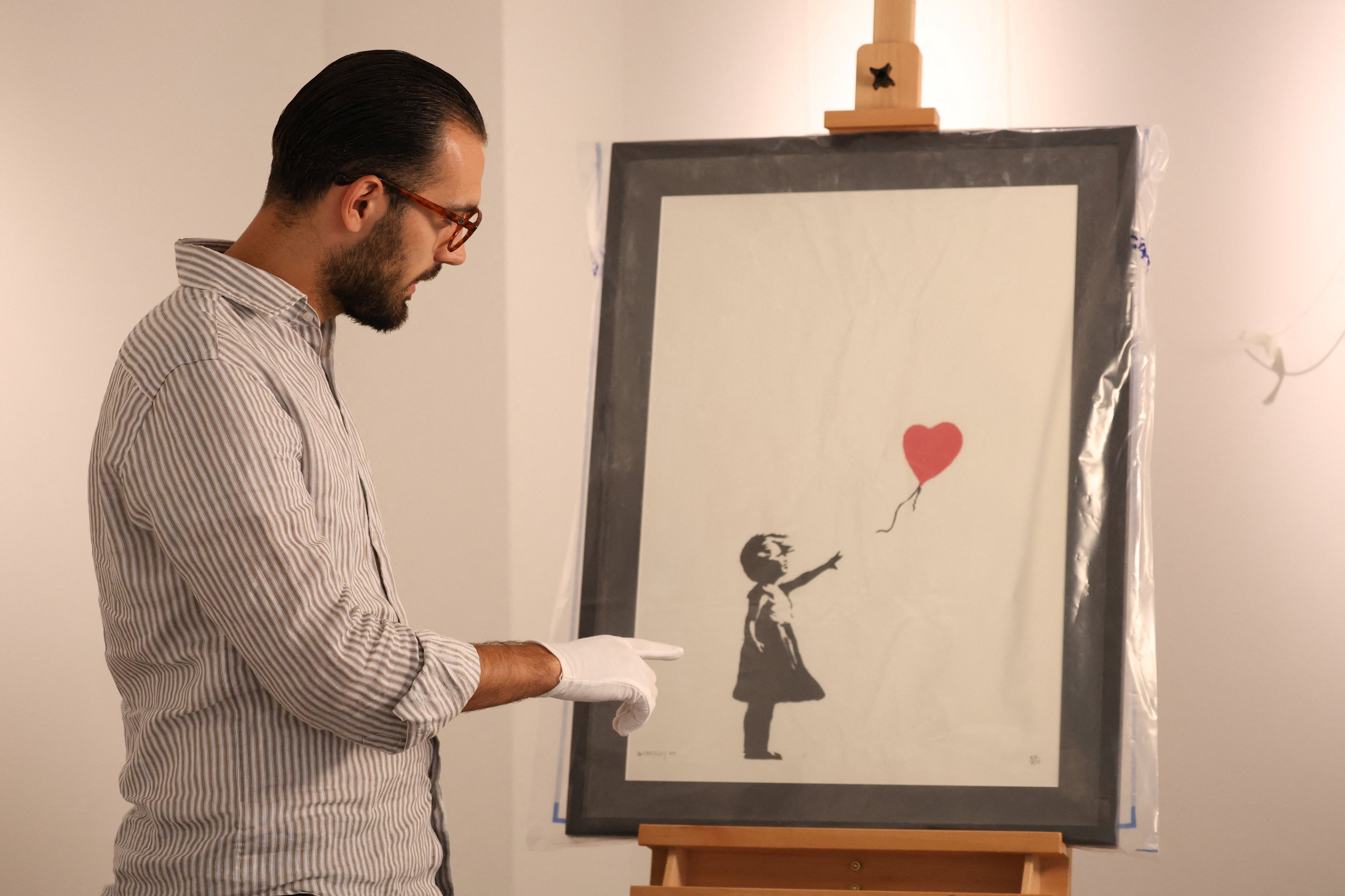 Gallery manager Lindor Mehmetaj points to Banksy's 'Girl with Balloon', which is seen in a police evidence bag at Grove Gallery where it was returned after being stolen, in London, Britain, September 13, 2024. REUTERS/Mina Kim NO RESALES. NO ARCHIVES.