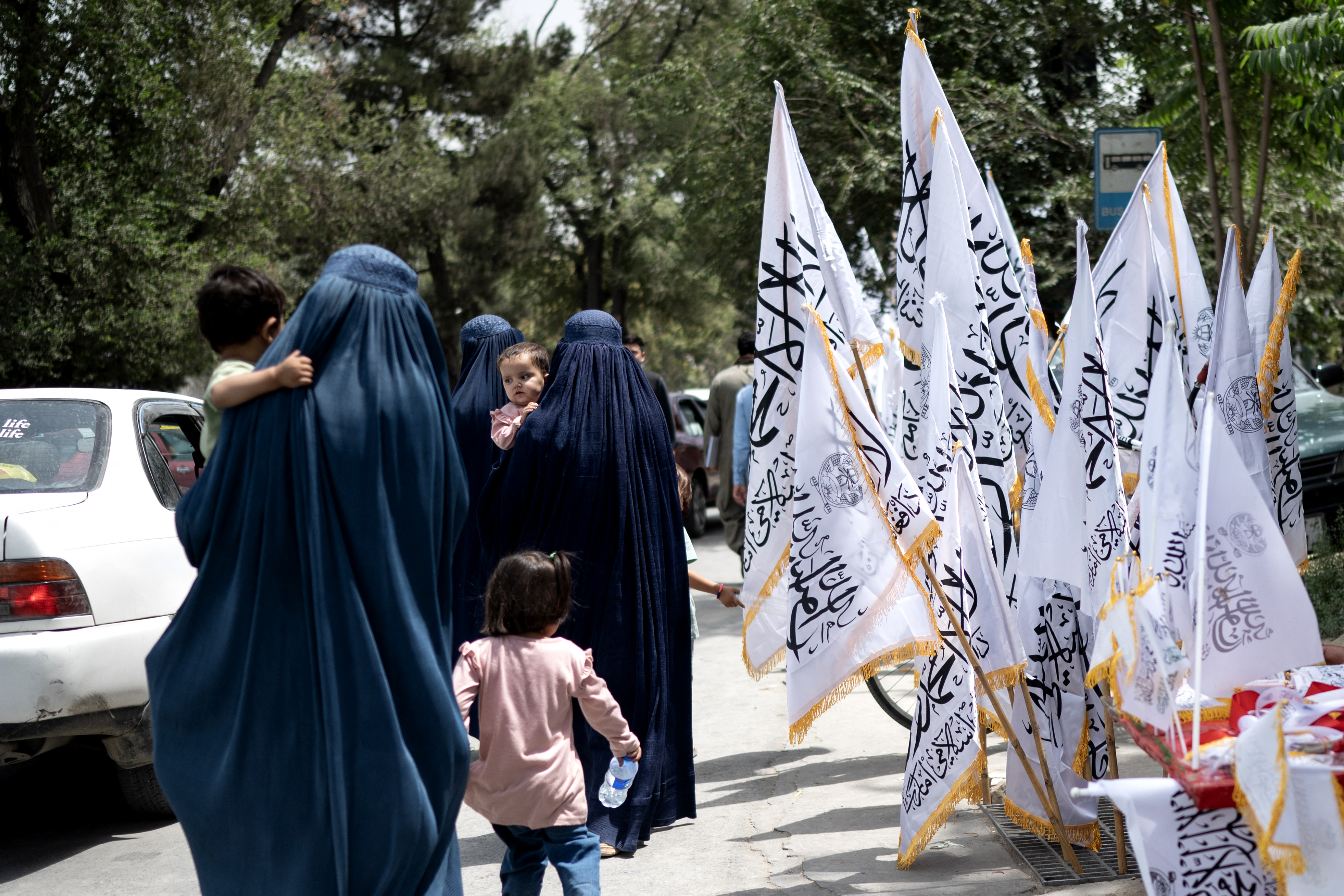 Afghan burqa-clad women walk past Taliban flags on the eve of fourth anniversary of the Taliban's takeover in 2021, in Kabul on August 14, 2025. (Photo by Wakil KOHSAR / AFP)