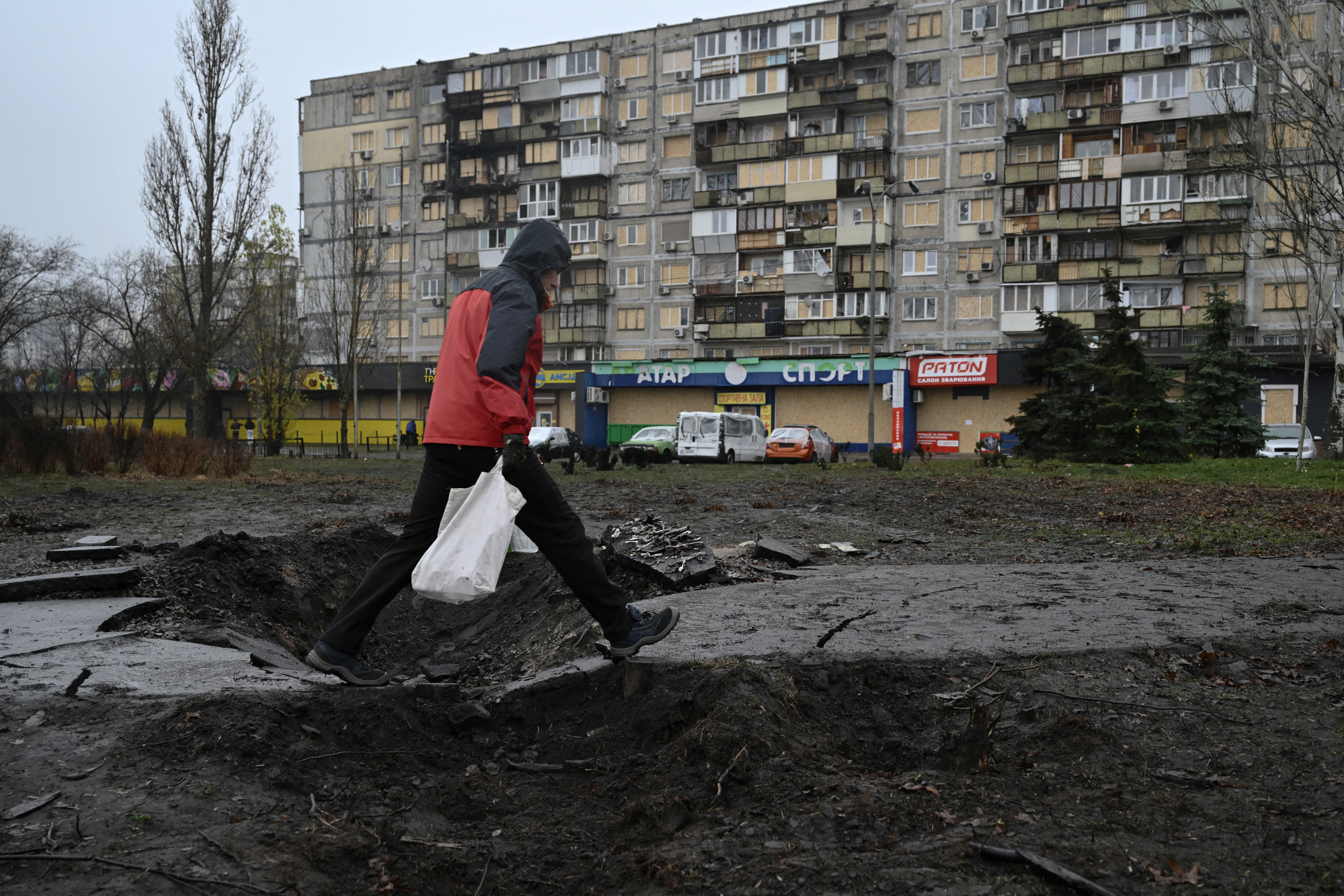 A man walks over a crater in front of a residential building damaged after a recent air attack, in Kyiv on December 3, 2025, amid the Russian invasion of Ukraine. (Photo by Genya SAVILOV / AFP)