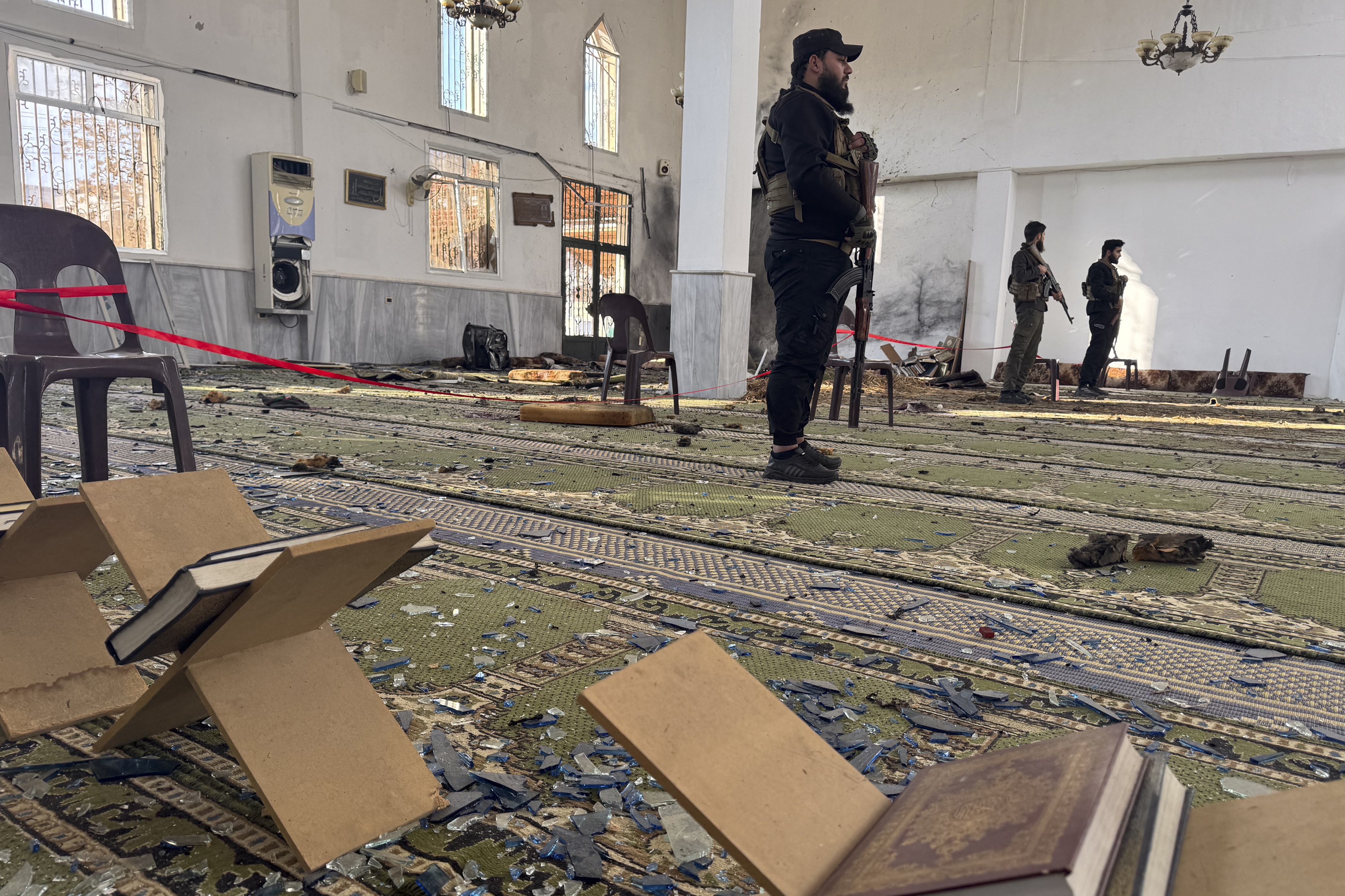 Armed men stand inside the Imam Ali ibn Abi Talib Mosque following an explosion in the Wadi al-Dahab neighborhood of Homs on December 26, 2025. A deadly explosion hit a mosque in a predominantly Alawite area of Syria's Homs on December 26, said authorities who reported at least six people killed. "A terrorist explosion targeted the Ali Bin Abi Talib Mosque during Friday prayers in Al-Khadri Street in the Wadi al-Dahab neighbourhood of Homs," the interior ministry said in a statement, adding that six people were killed and 21 others wounded. (Photo by Omar HAJ KADOUR / AFP)