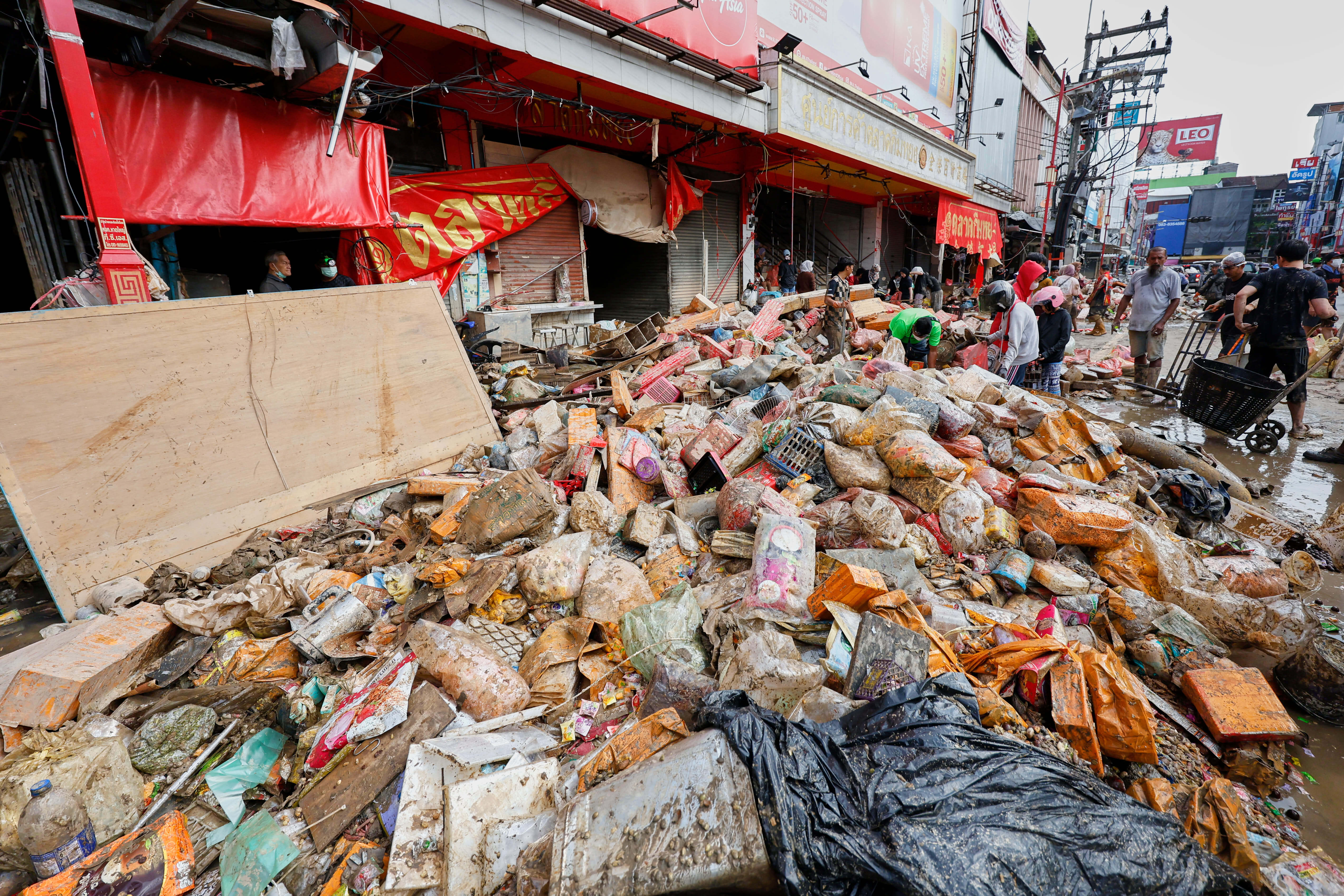 People walk near goods damaged from floods in Songkhla province, southern Thailand, Saturday, Nov. 29, 2025.