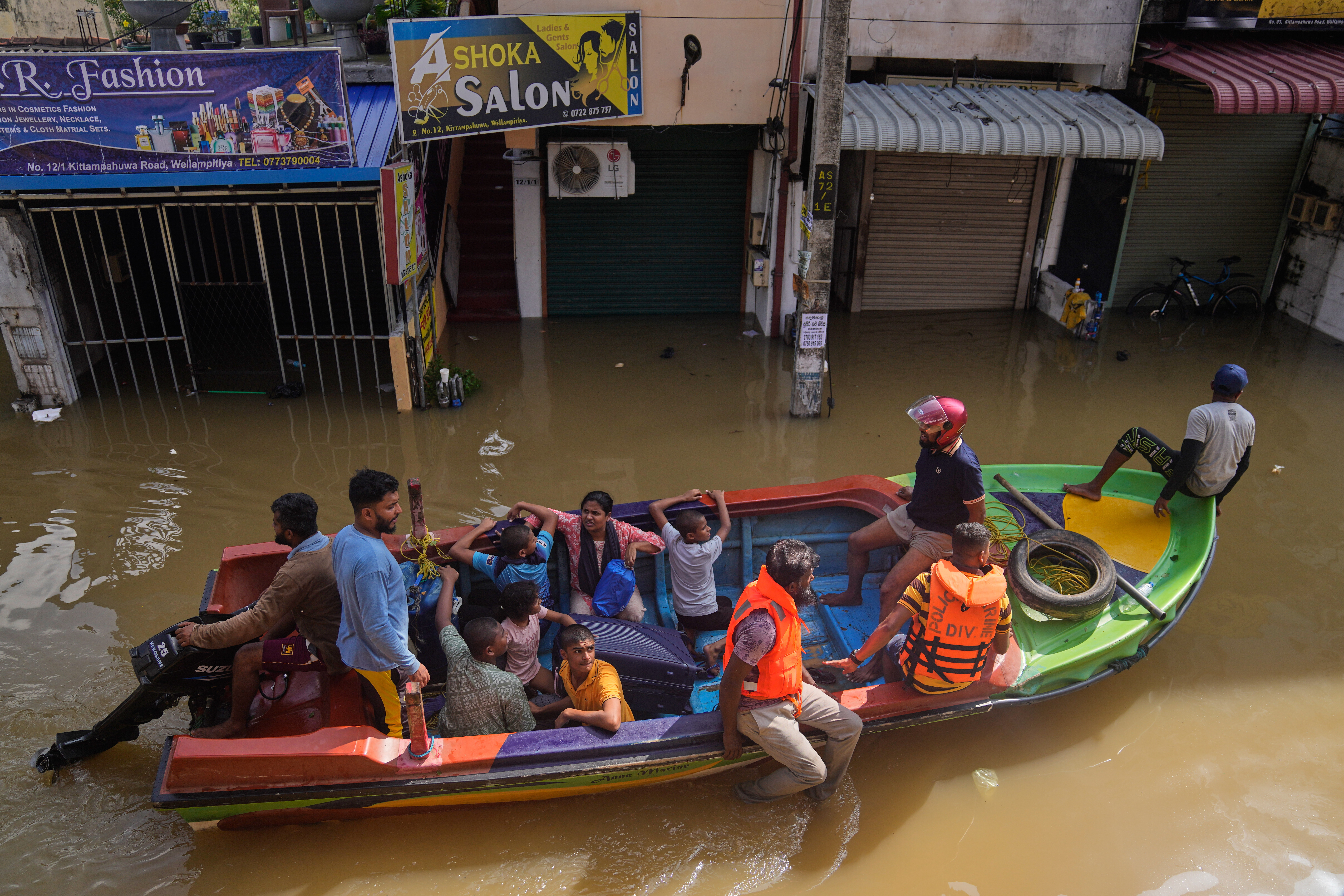 Rescuers move people to safety on a small boat in a flooded area.