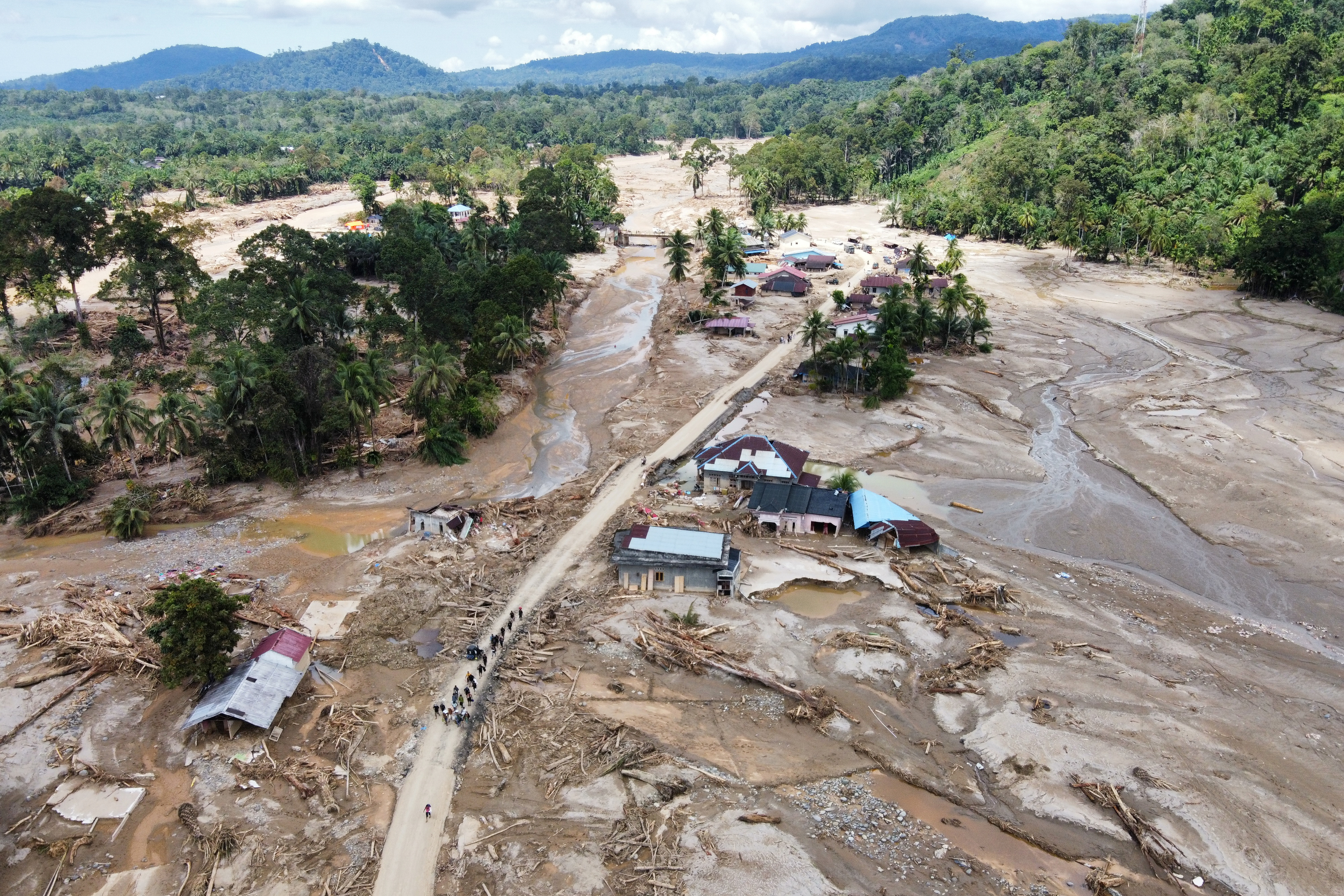 People walk along a flooded road in a village.