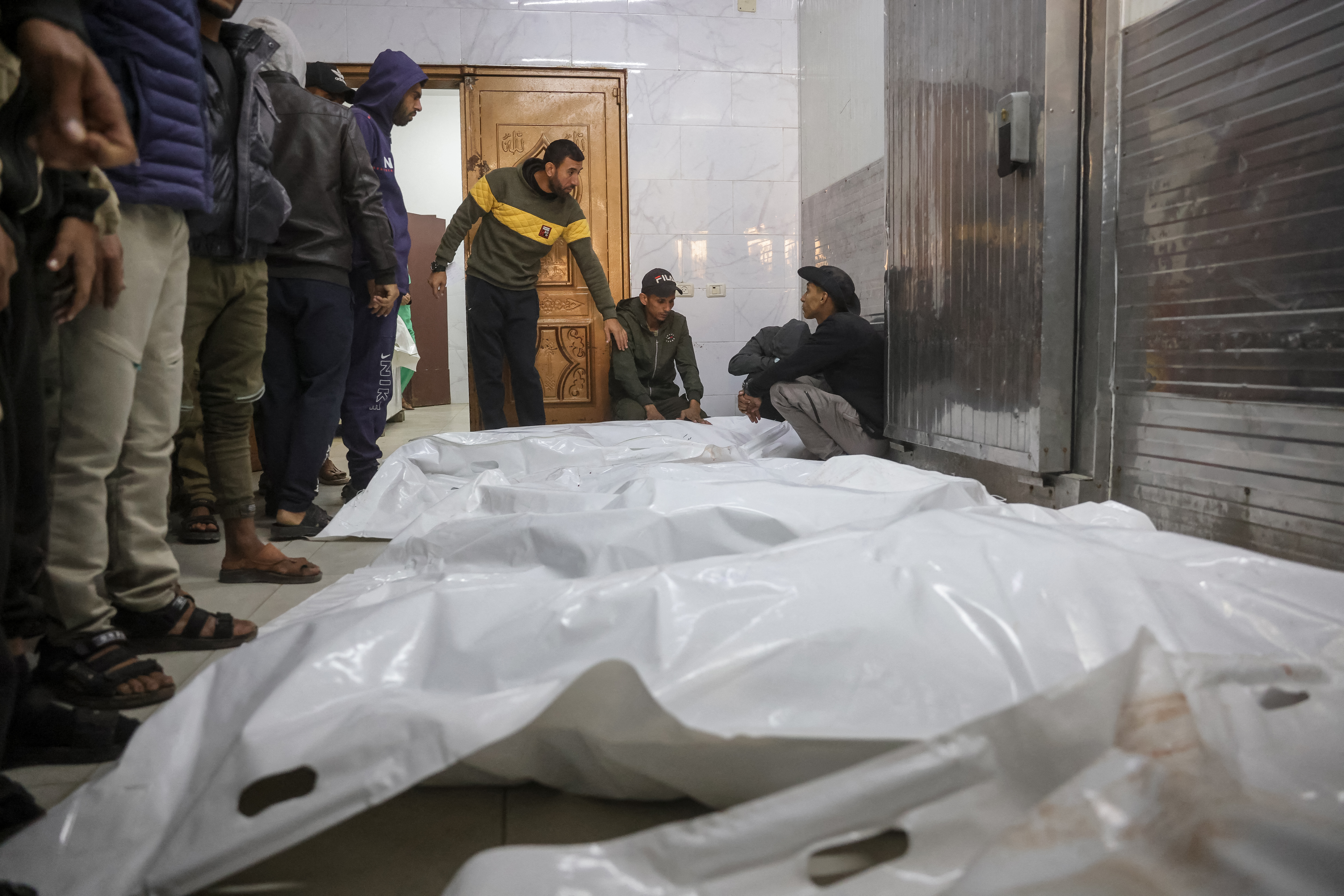 People stand next to white body bags while attending the funeral of Palestinians killed on December 3, by an Israeli strike, at Nasser Hospital in Khan Yunis, southern Gaza Strip on December 4, 2025.