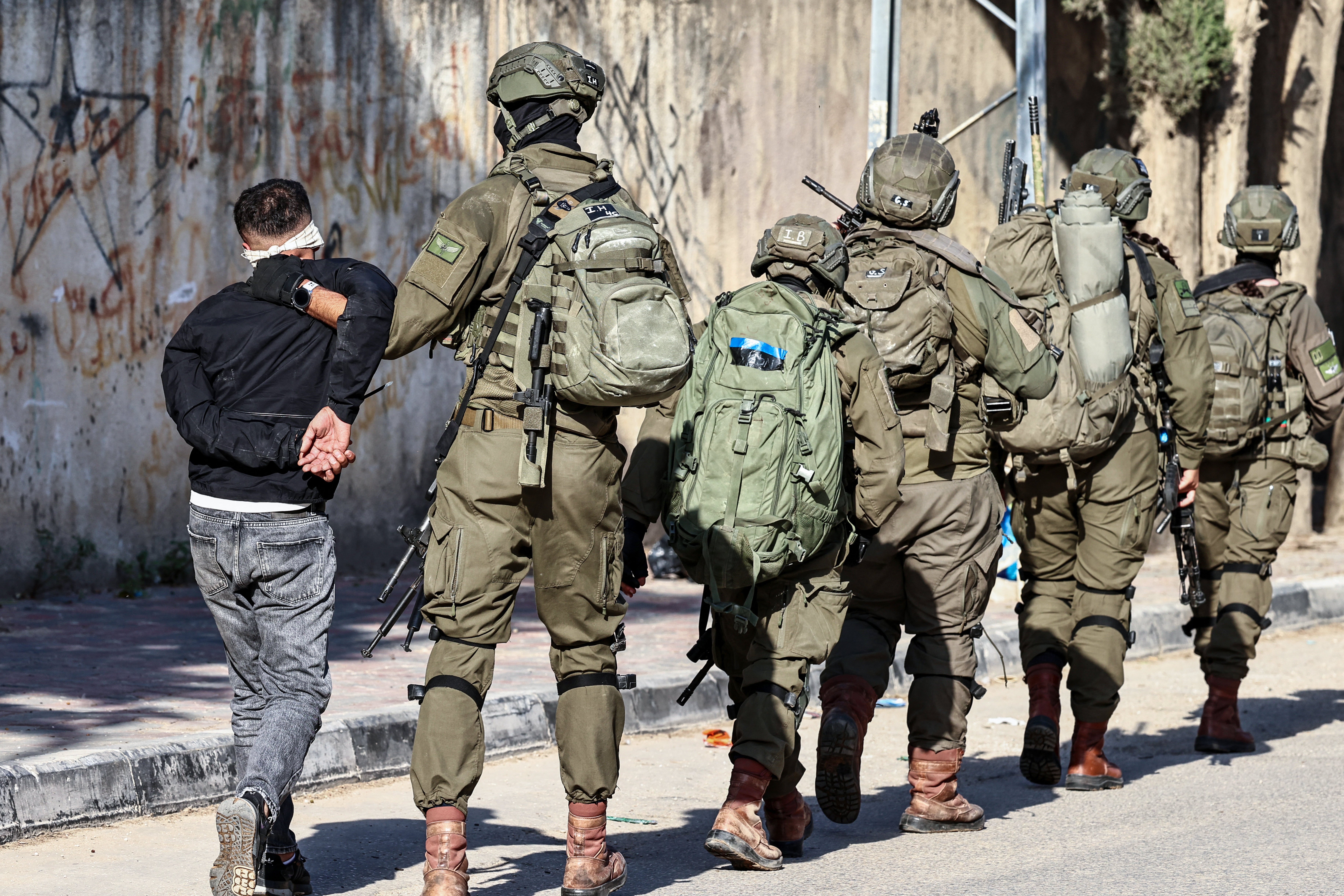 TOPSHOT - Israeli soldiers detain a Palestinian man during a military operation in the town of Qalqiya, in the occupied West Bank on December 4, 2025.