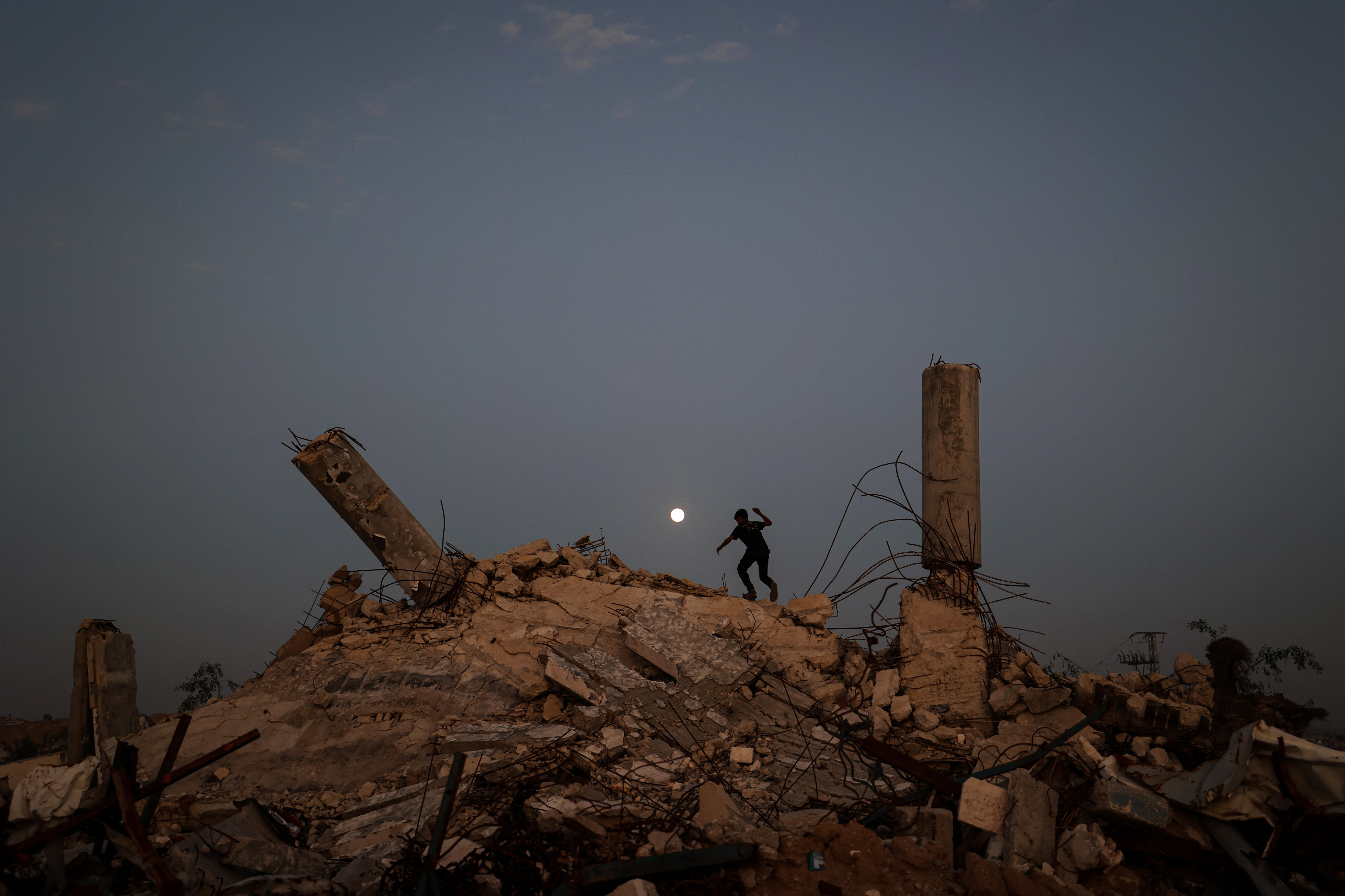 TOPSHOT - A youth plays on the rubble of a destroyed building as the Cold Moon, the last supermoon of the year, rises over the Nuseirat camp for displaced Palestinians in the central Gaza Strip on December 4, 2025.