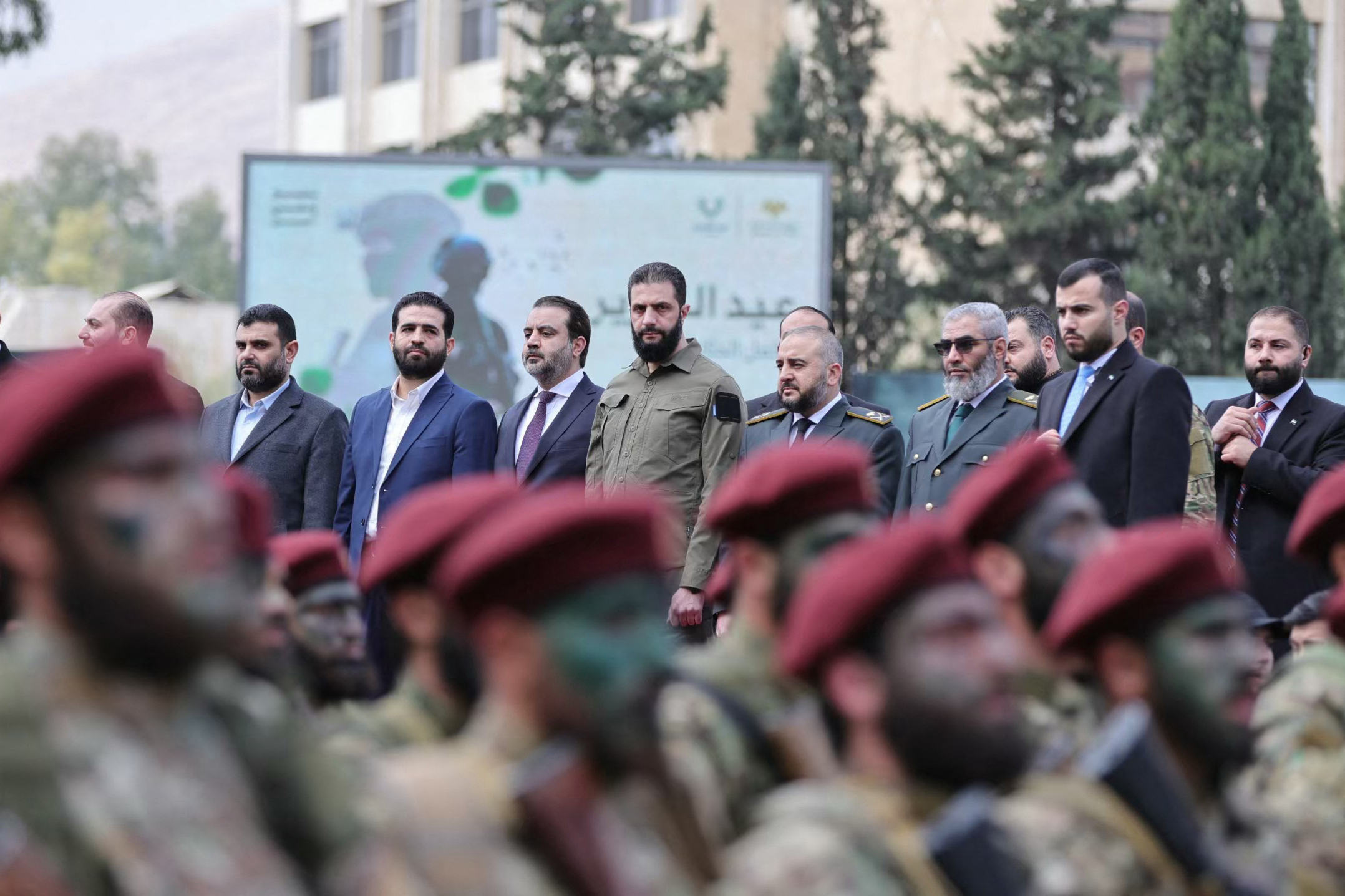 This handout photograph released by the official Syrian Arab News Agency (SANA) on December 8, 2025, shows Syria's President Ahmed al-Sharaa (C) and Syrian Minister of Foreign Affairs and Expatriates Asaad Al-Shaibani (4th L) observing the military parade in Damascus during the anniversary of the ousting of longtime ruler Bashar al-Assad.
