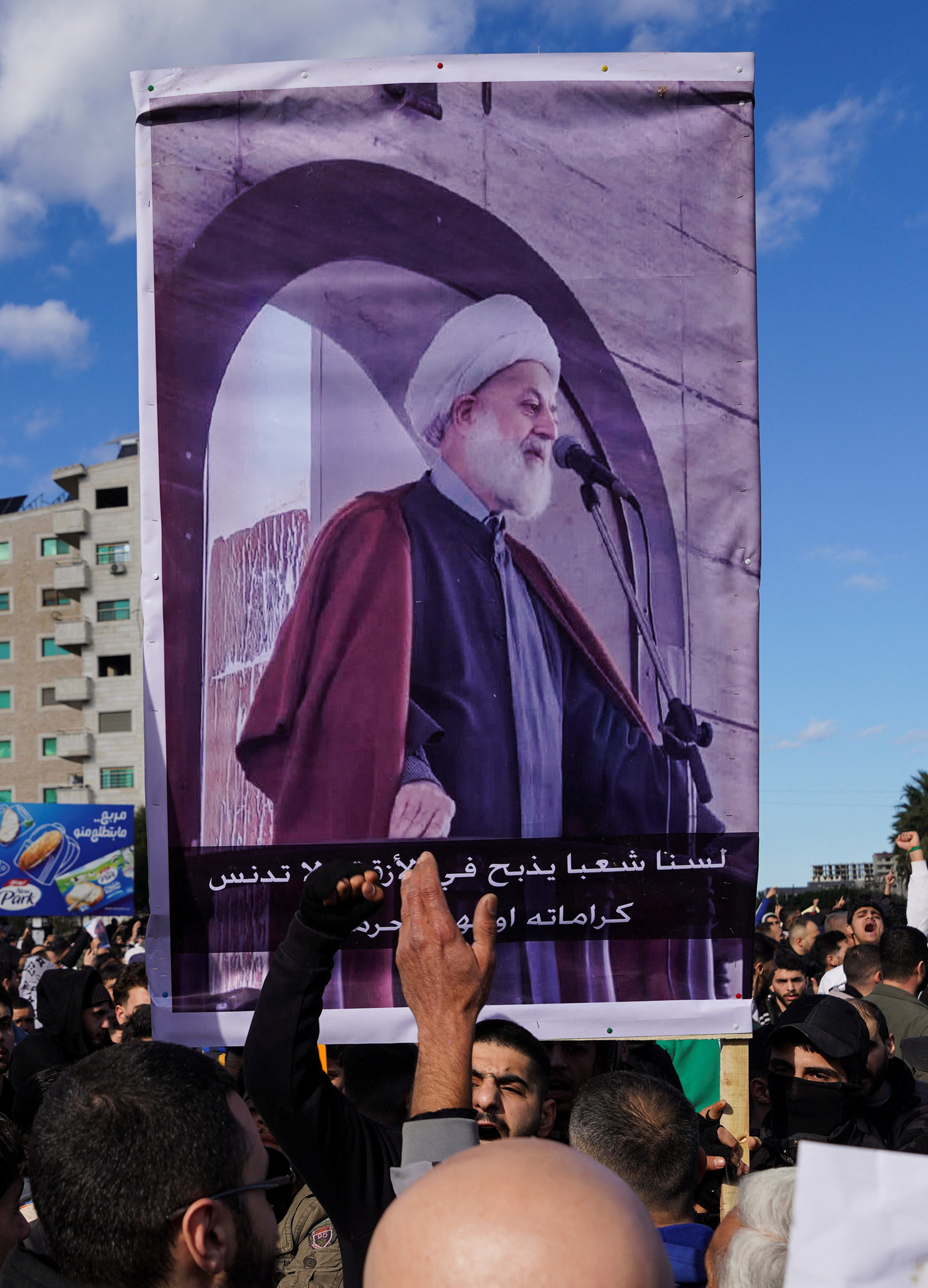 People from the Alawite sect hold up a poster with the image of the head of the Supreme Alawite Islamic Council, Ghazal Ghazal, during a protest, as they demand federalism and an end to what they say is the killing and violations against Alawites, in Latakia, Syria, December 28, 2025. REUTERS/Karam al-Masri